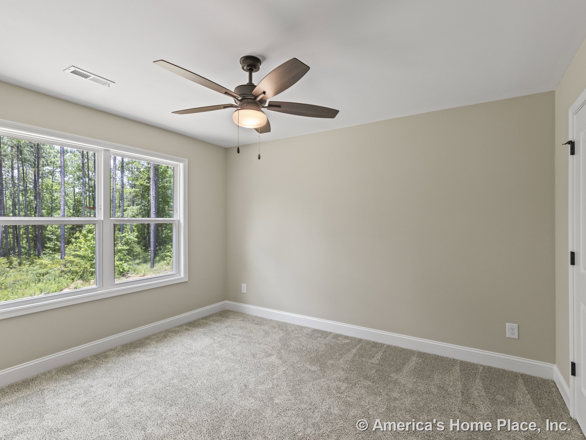 Beige carpeted bedroom with double windows framed in white trim, ceiling fan and light fixture, neutral painted walls, white baseboards, and interior door featuring black hardware