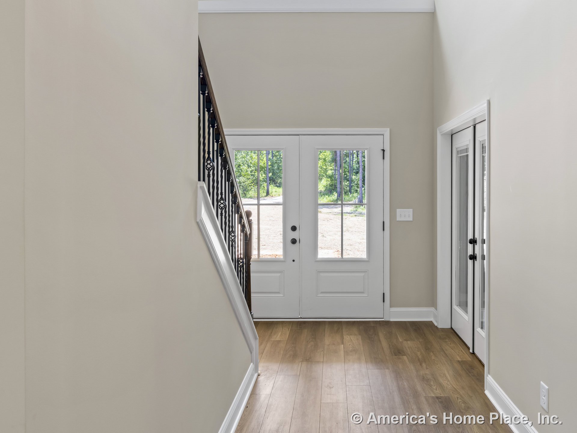 Double front door with glass panels, wood plank flooring, staircase with iron balusters, neutral wall paint, white trim and baseboards, interior glass door, high ceiling, and
