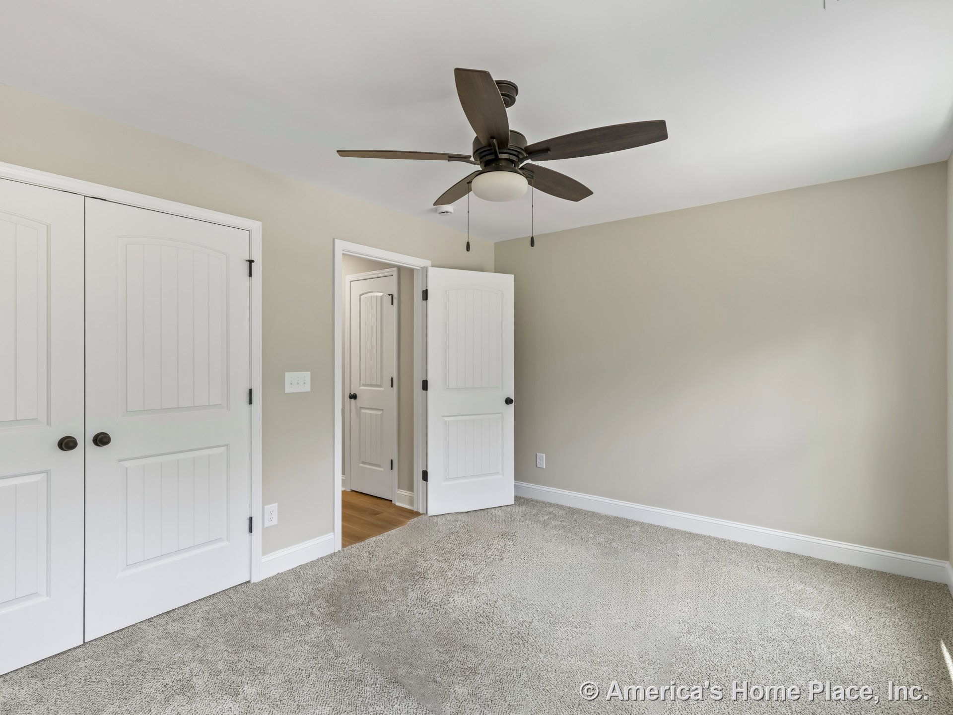 Carpeted bedroom with white paneled closet doors, ceiling fan and light fixture, neutral wall color, white trim and baseboards, and matching paneled interior door.