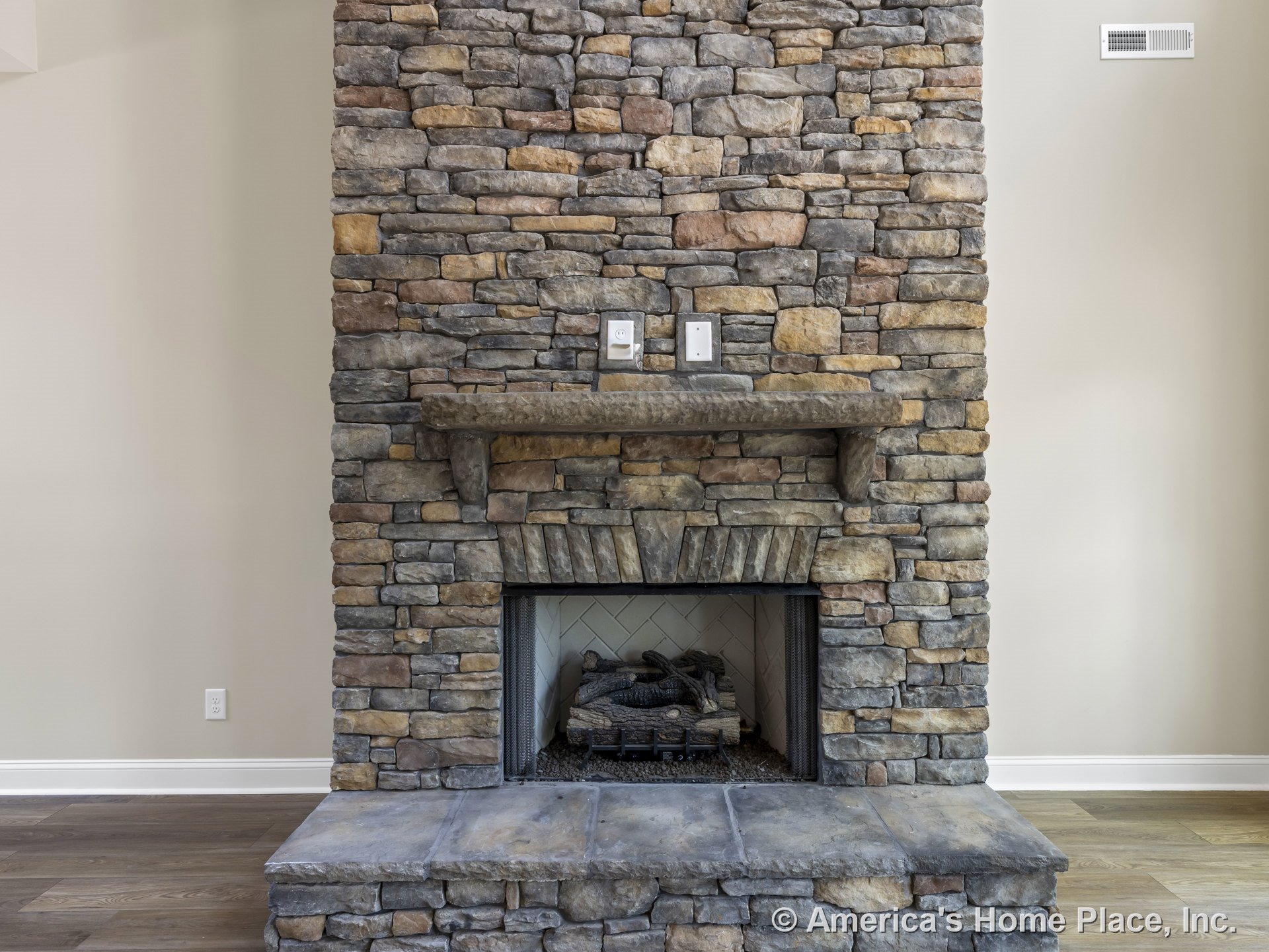 Floor-to-ceiling stacked stone fireplace with raised stone hearth, wood mantel shelf, gas insert, wood plank flooring, and neutral painted walls.