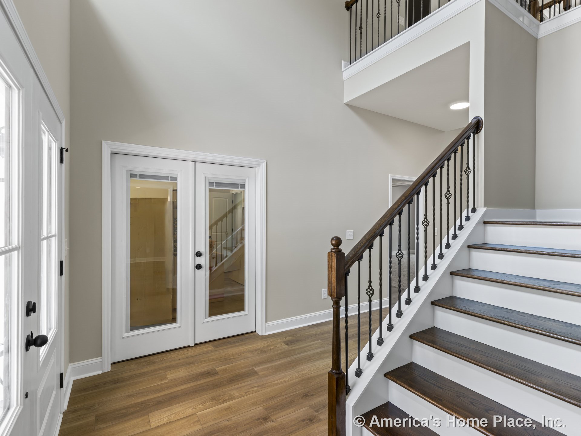 Hardwood foyer with double glass doors, staircase featuring dark wood treads and iron balusters, white trim and baseboards, and open ceiling design
