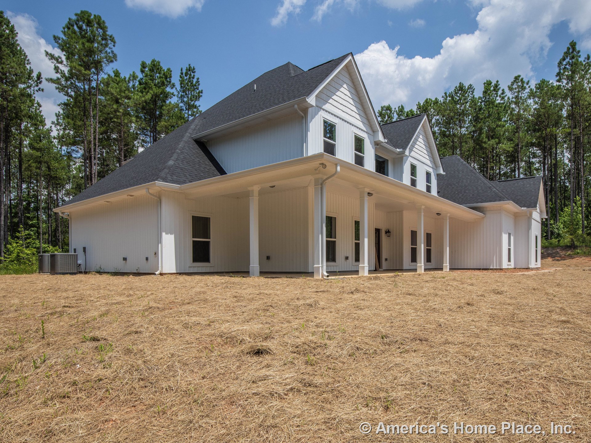 Large covered rear porch with white vertical board and batten siding, multiple double-hung windows, black shingle roof, prominent gabled rooflines, exterior lighting fixtures, and