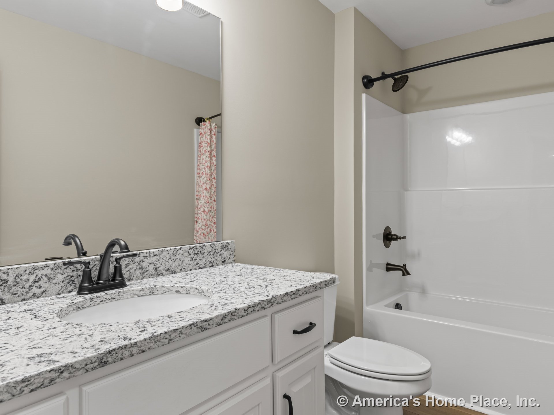 Granite vanity countertop with white shaker cabinets, large wall mirror above single sink, tub-shower unit featuring oil-rubbed bronze faucet and shower hardware, light wood