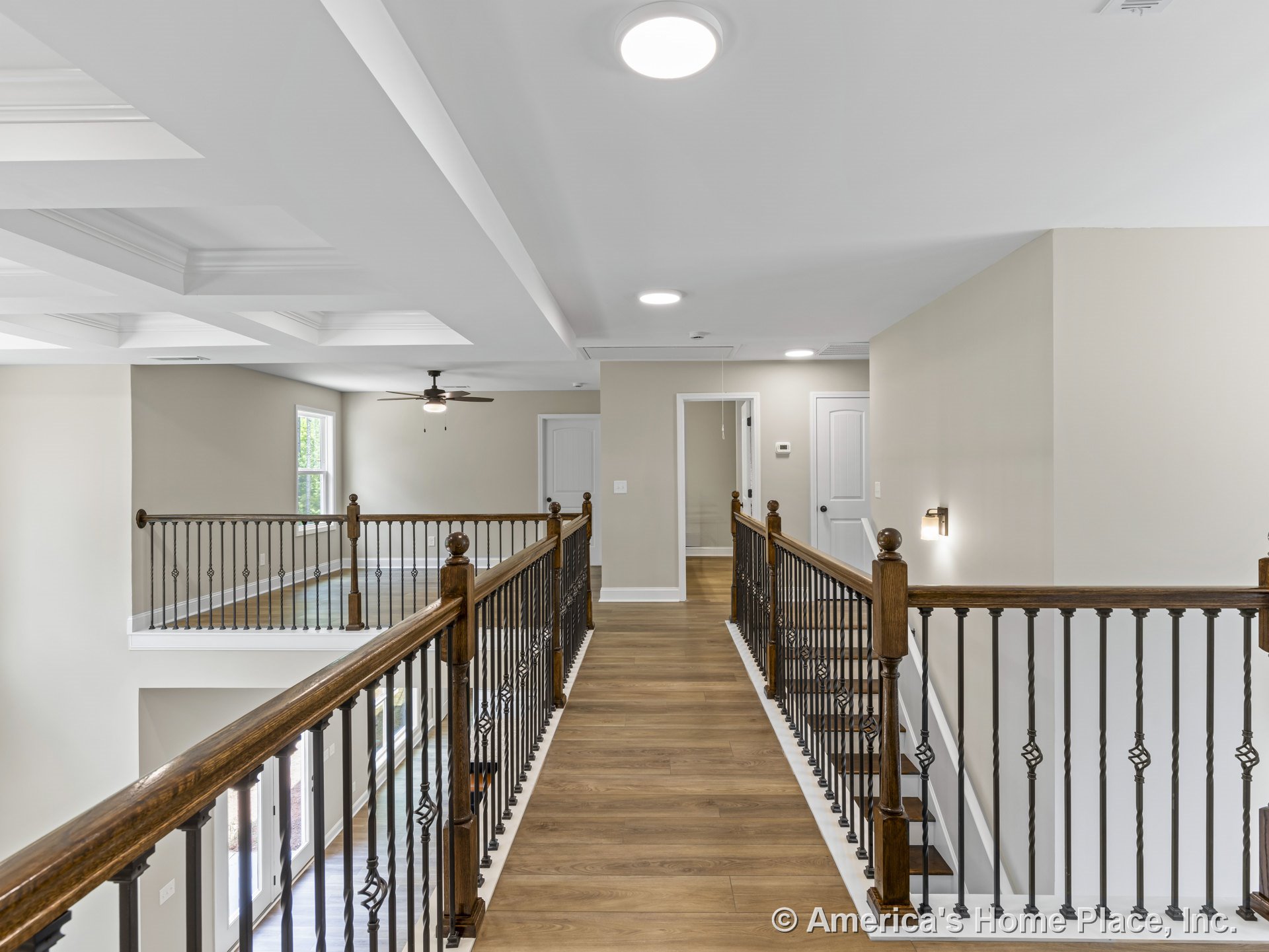 Upstairs hallway with wood flooring, iron balusters and wood handrails, tray ceiling with recessed lights, wall sconces, white baseboards and trim, multiple interior doors