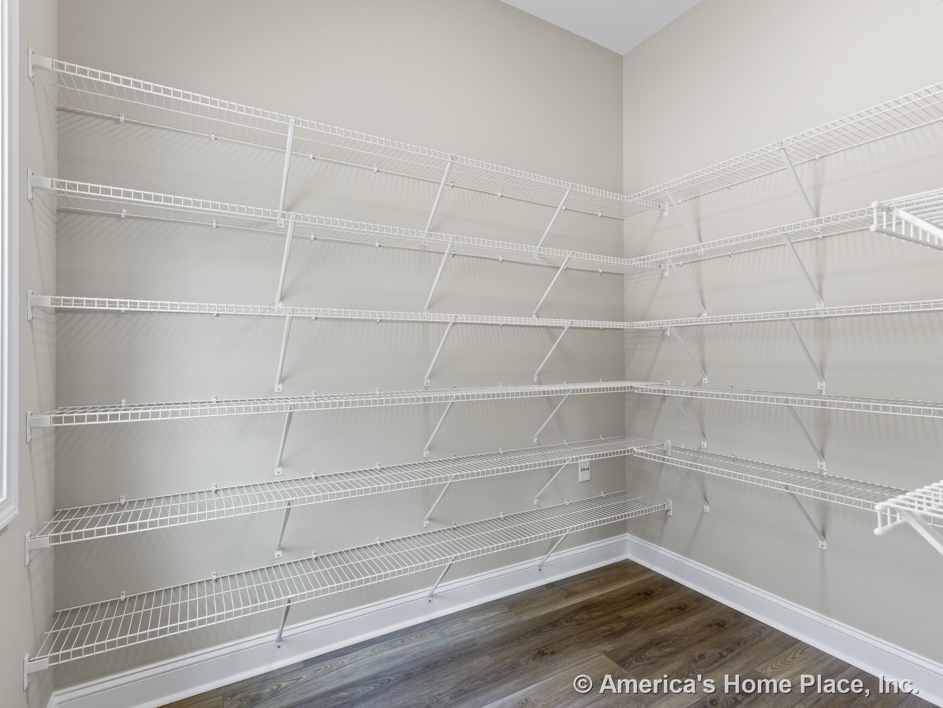 Walk-in pantry with multiple rows of built-in white wire shelving, wood-look flooring, neutral painted walls, baseboard trim, and a window with decorative trim.