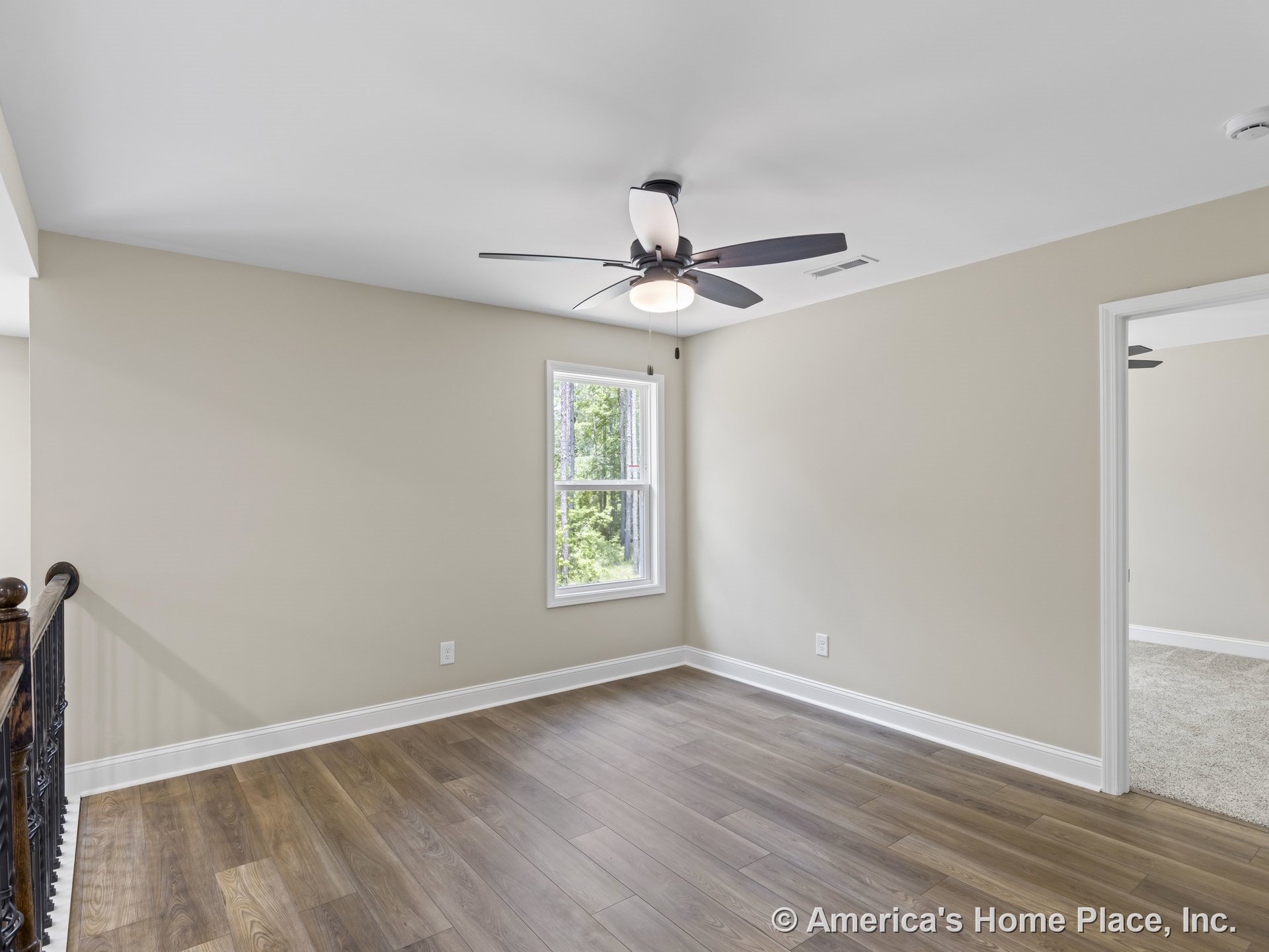 Upstairs loft with wood-look plank flooring, ceiling fan with integrated light, single window framed in white trim, neutral painted walls, white baseboards, and open doorway
