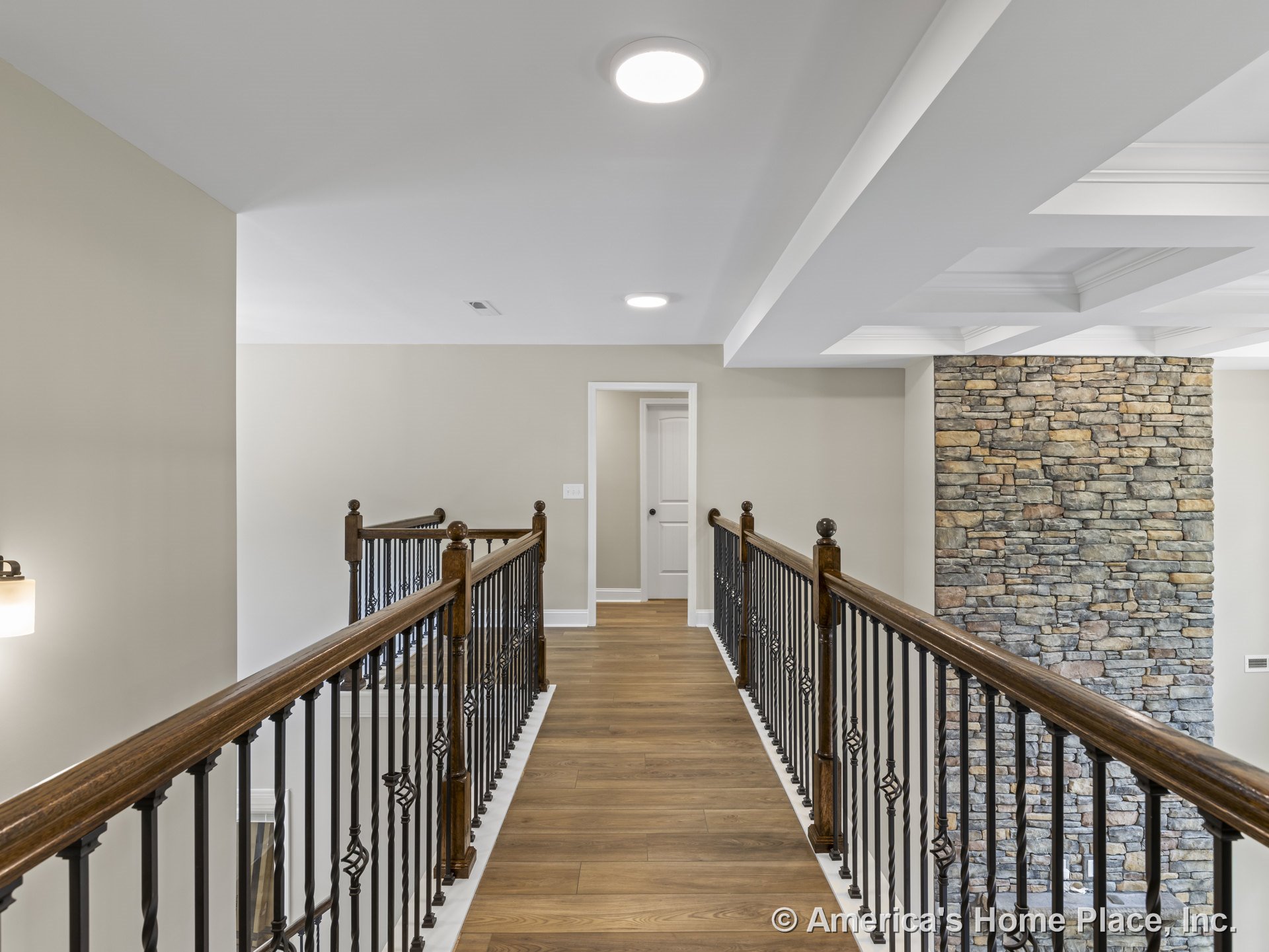 Hallway with wood flooring, wrought iron balusters and wood handrails, stone accent wall, tray ceiling detail, recessed lighting, and neutral painted walls.