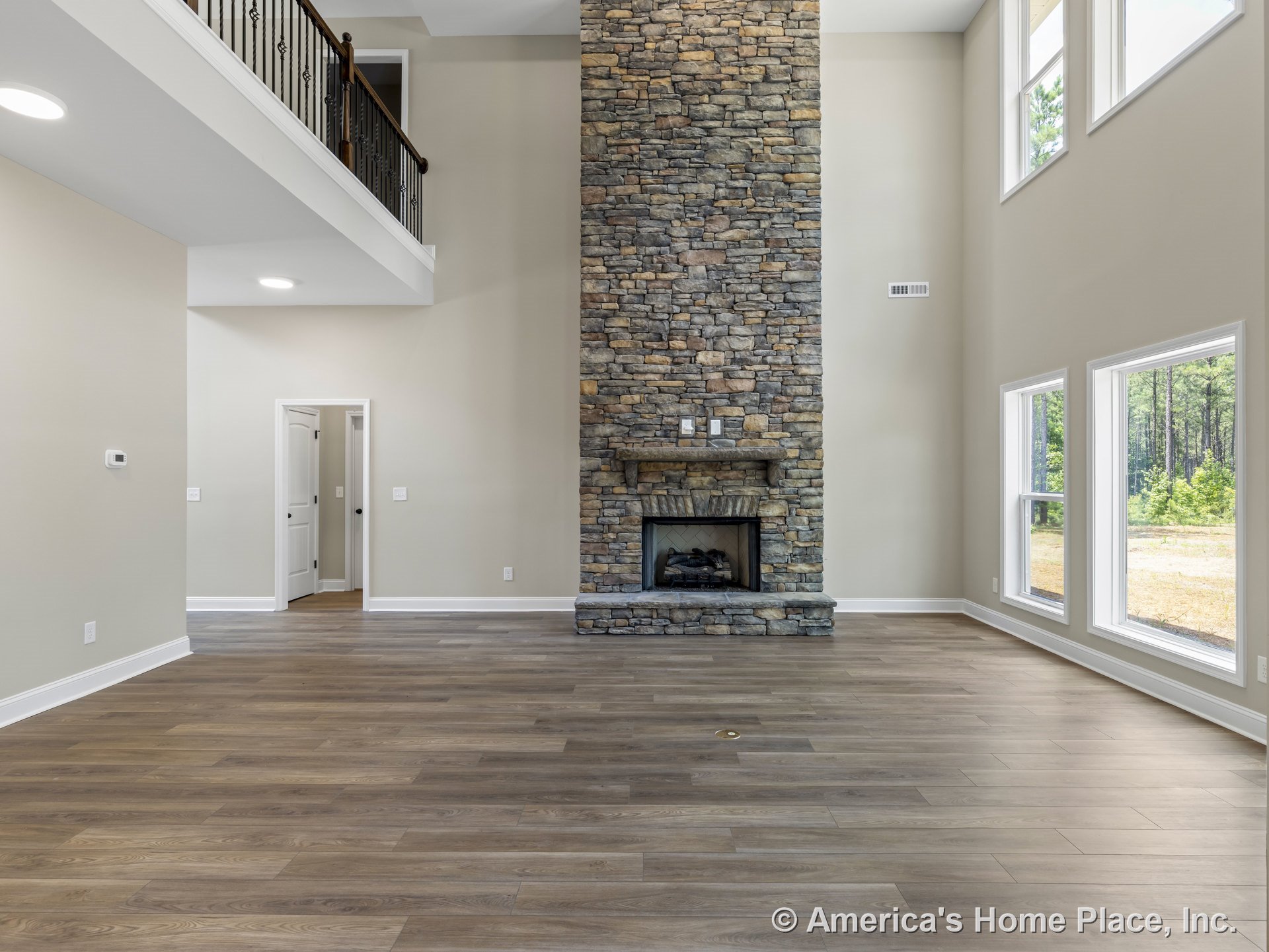 Floor-to-ceiling stone fireplace anchors the living room with double-height ceiling, expansive windows, wood-look plank flooring, white trim, and open balcony railing overlooking