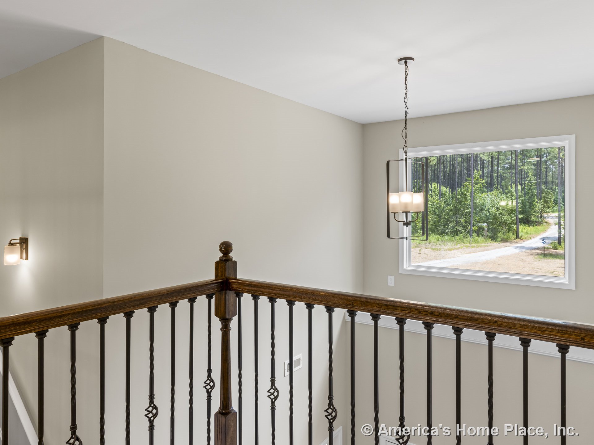 Stair landing with iron baluster railing, wood handrail, large window framed in white trim, pendant ceiling light, wall sconce lighting, and neutral painted walls.