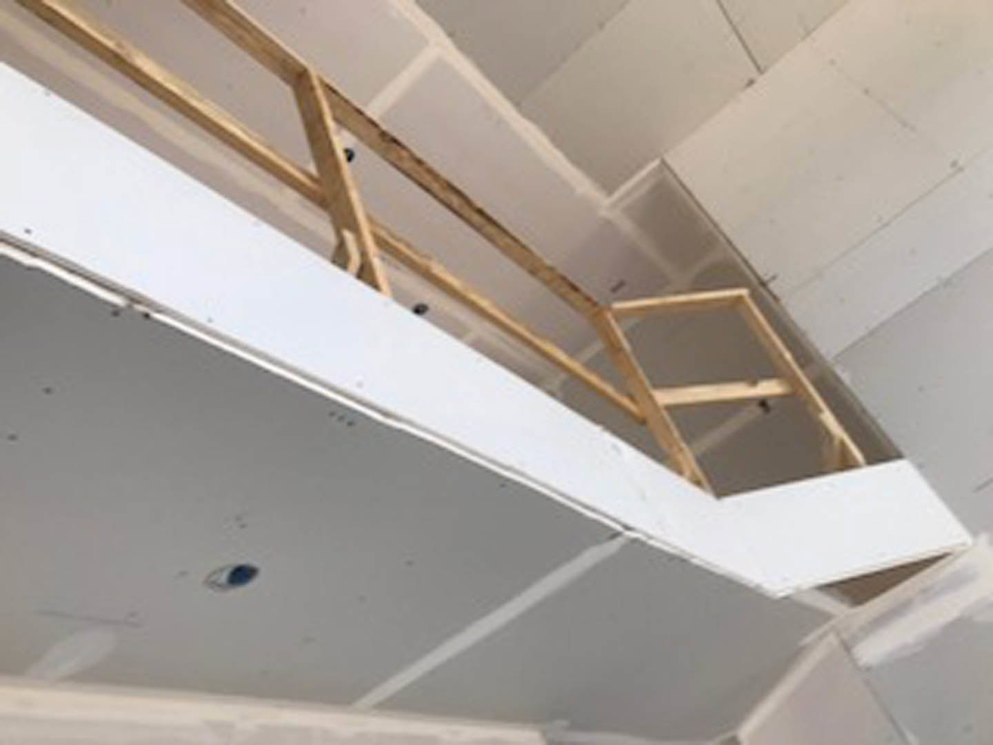 Wooden ladder leaning against white plaster ceiling with exposed wooden beams in a bright indoor space