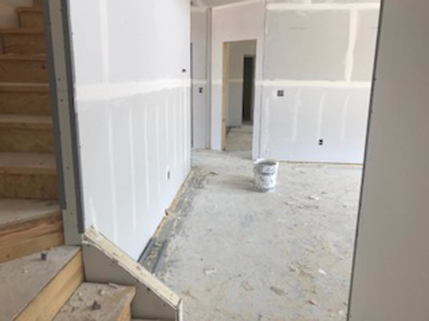 White-walled room with a white paint bucket on light wooden plank flooring, white door and trim visible