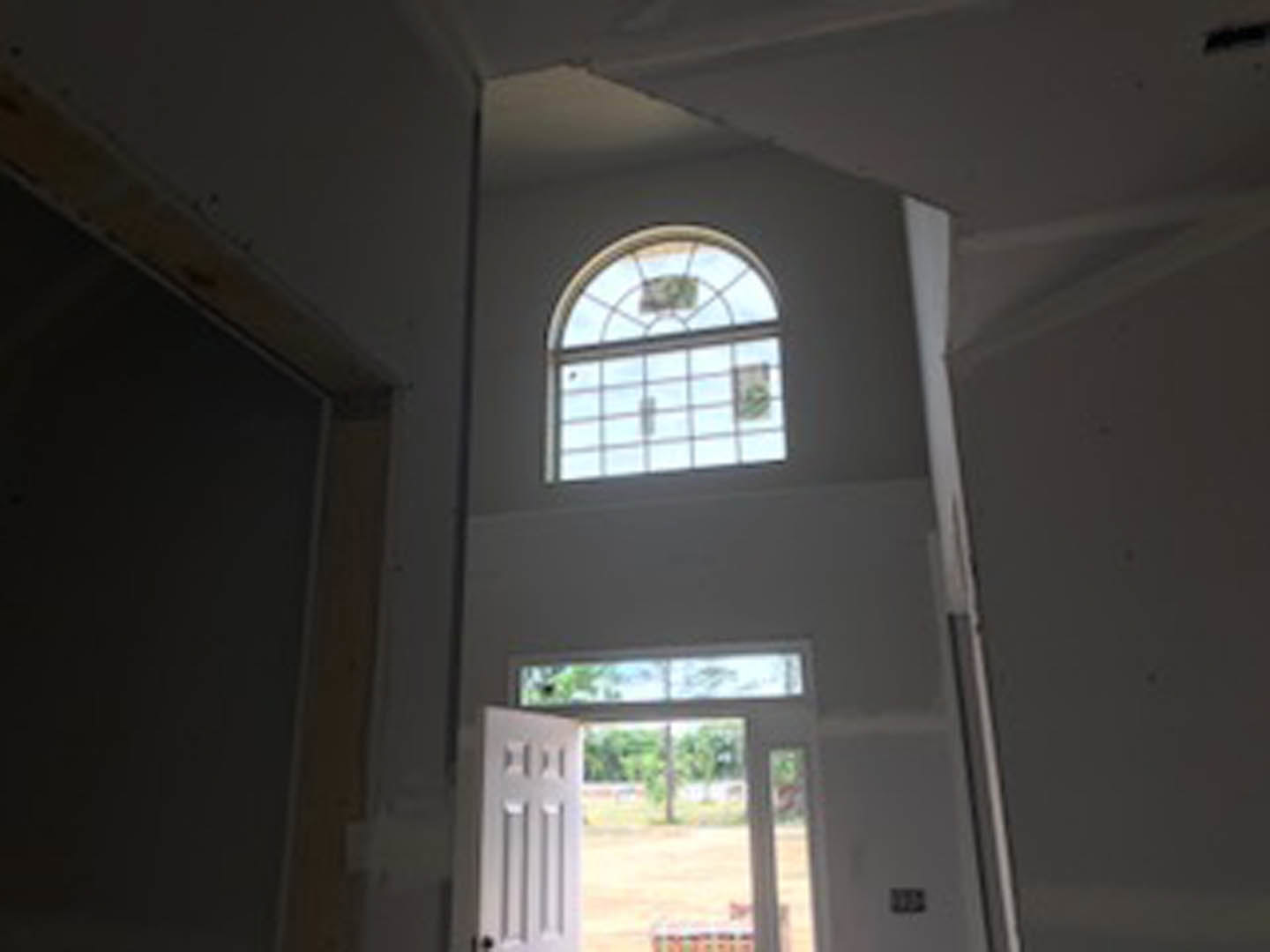 White-walled room with open white door leading to a grassy yard, rectangular window with black trim, simple molding, and natural daylight illuminating the interior.