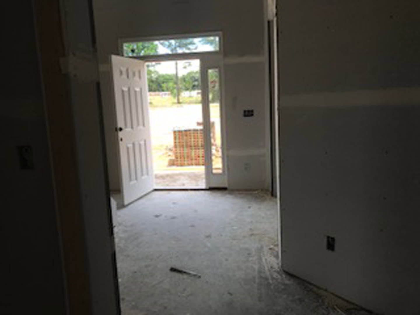 White door with glass panels open to a room with light-colored flooring, white walls, and a window letting in natural light; black rectangular fixture mounted on wall near door.