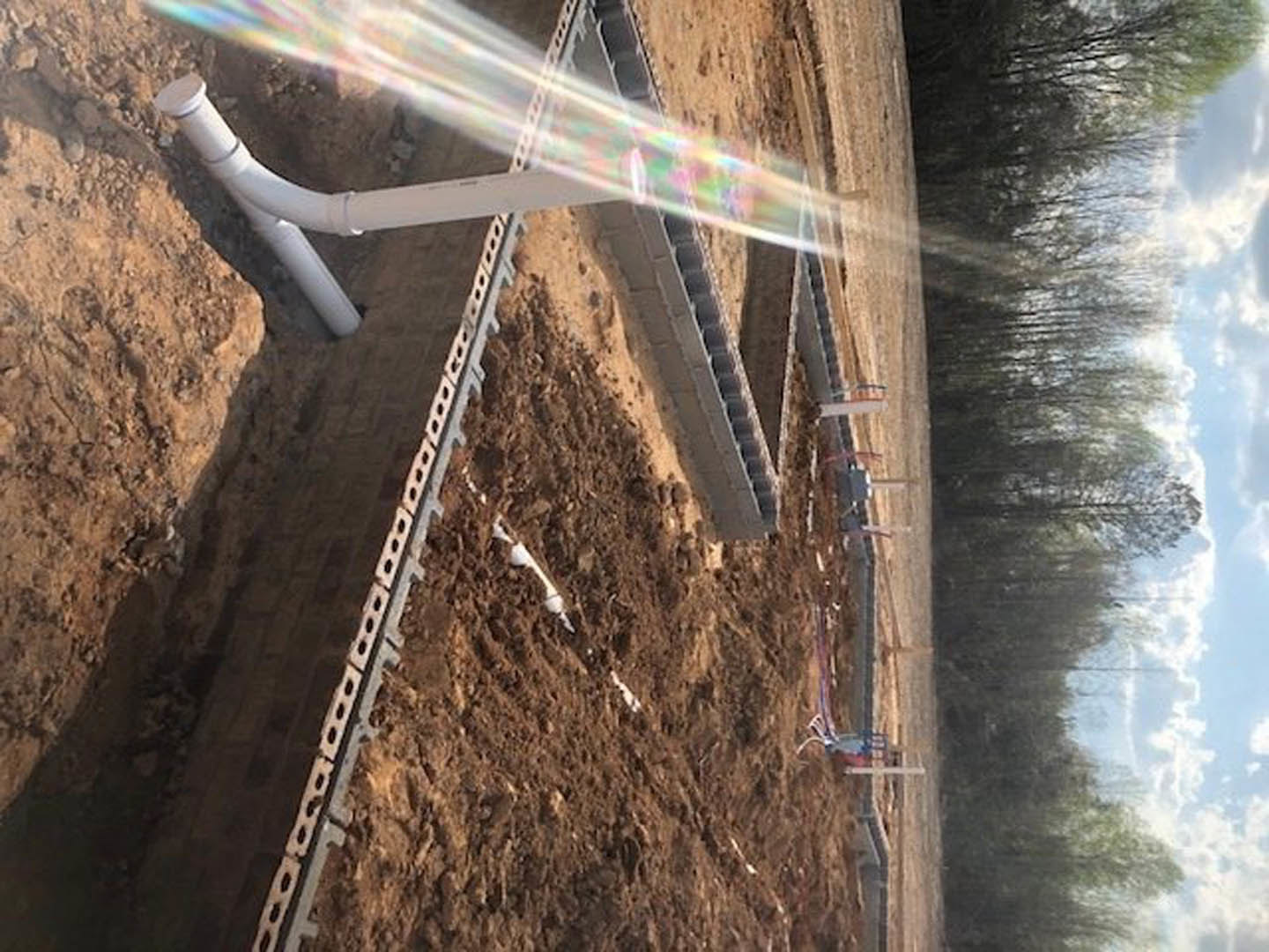 Sprinkler attached to white pipe spraying water across outdoor ground with mountain and sky in background