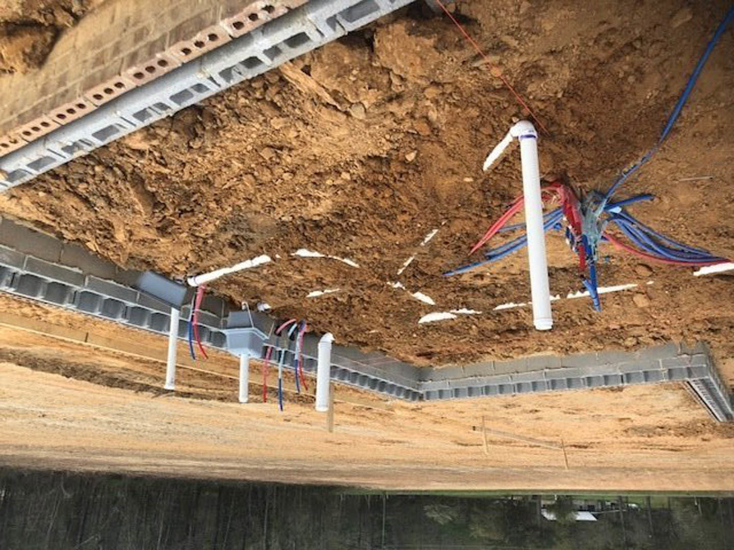 Exposed pipes and electrical wires emerging from a hole in the ground at an outdoor residential construction site