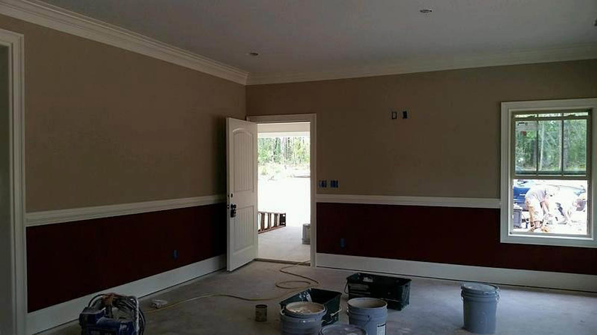 Unfinished room with concrete floor, scattered paint buckets, white door, and window showing person outside