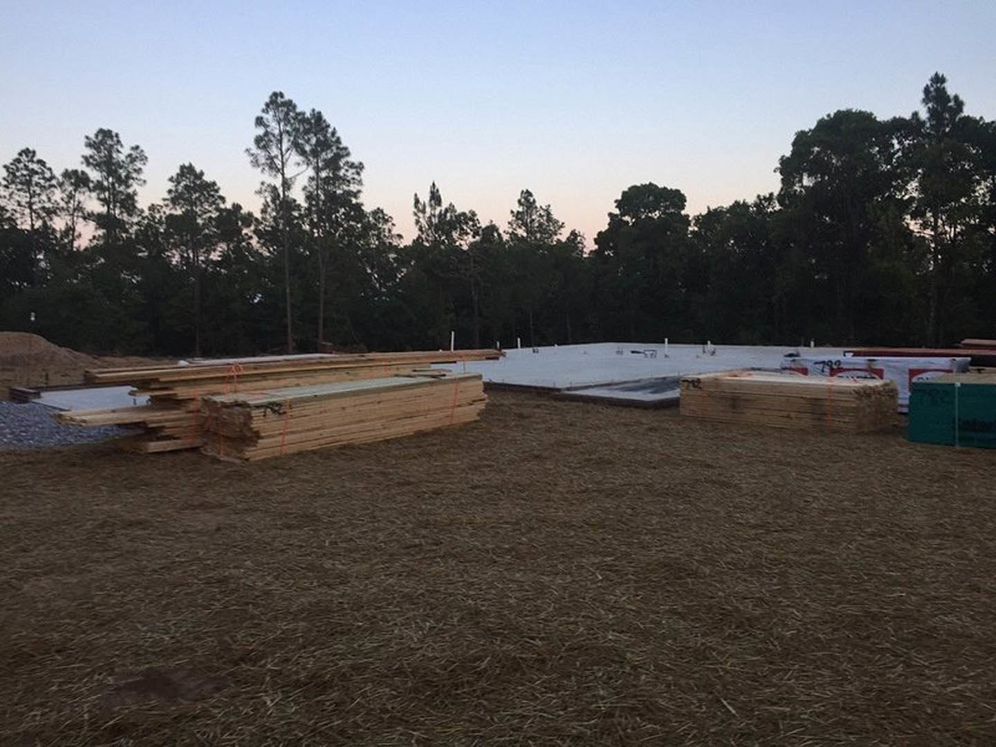 Stack of wood planks on grassy field with trees in background, clear sky overhead