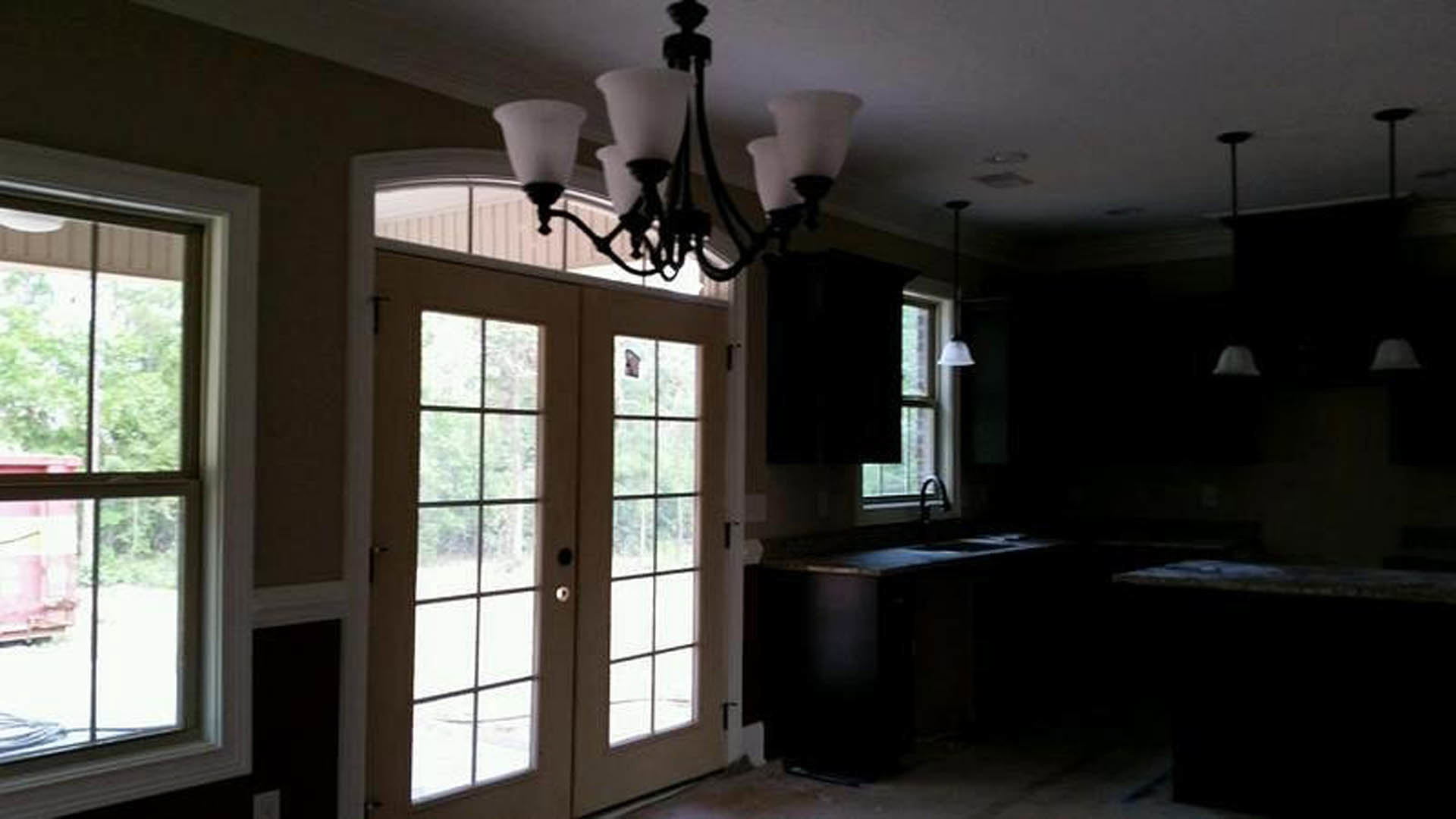 Modern kitchen with dark countertops, large window overlooking trees, and a contemporary chandelier hanging from the ceiling.