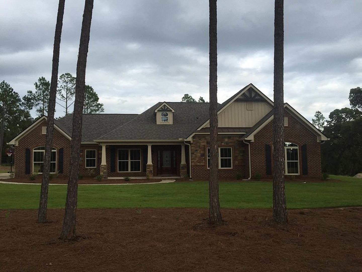 Two-story house with white-trimmed windows, glass panel front door, dormer on the roof, surrounded by mature trees and green lawn