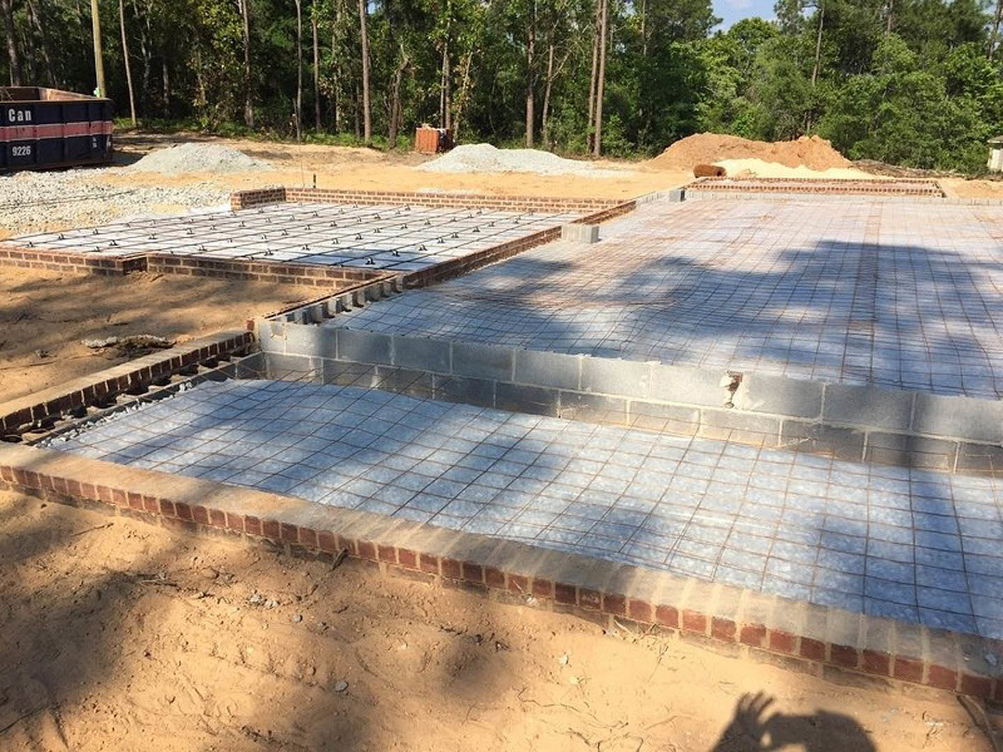 Concrete foundation with wire mesh at a construction site, surrounded by dirt and trees