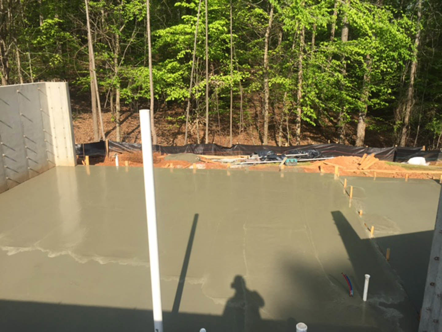 Concrete slab foundation with person’s shadow cast on the surface, surrounded by dense trees in the background, illuminated by natural light