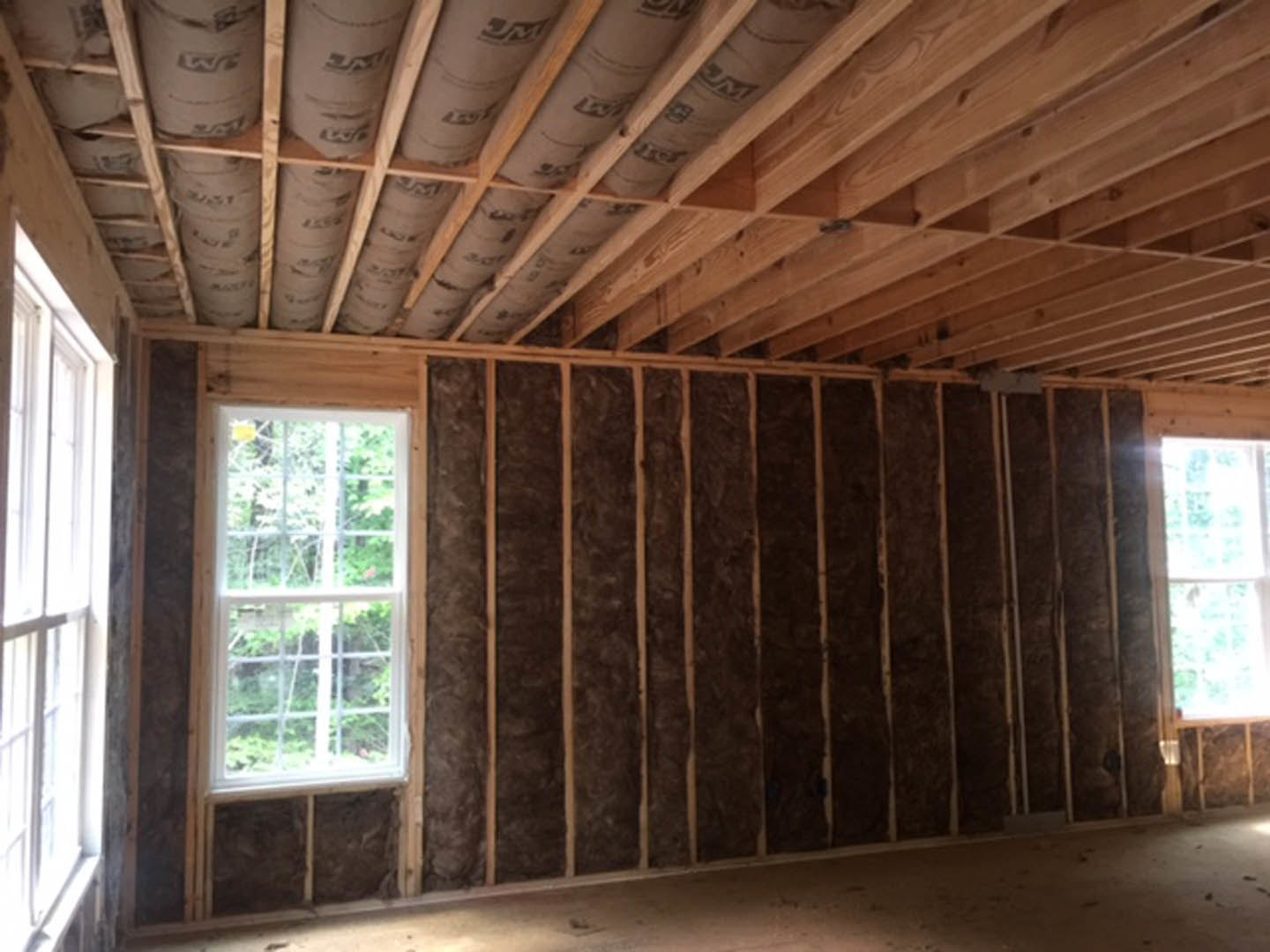 Room with large window overlooking trees, wood plank wall, exposed wooden ceiling beams, and visible piping