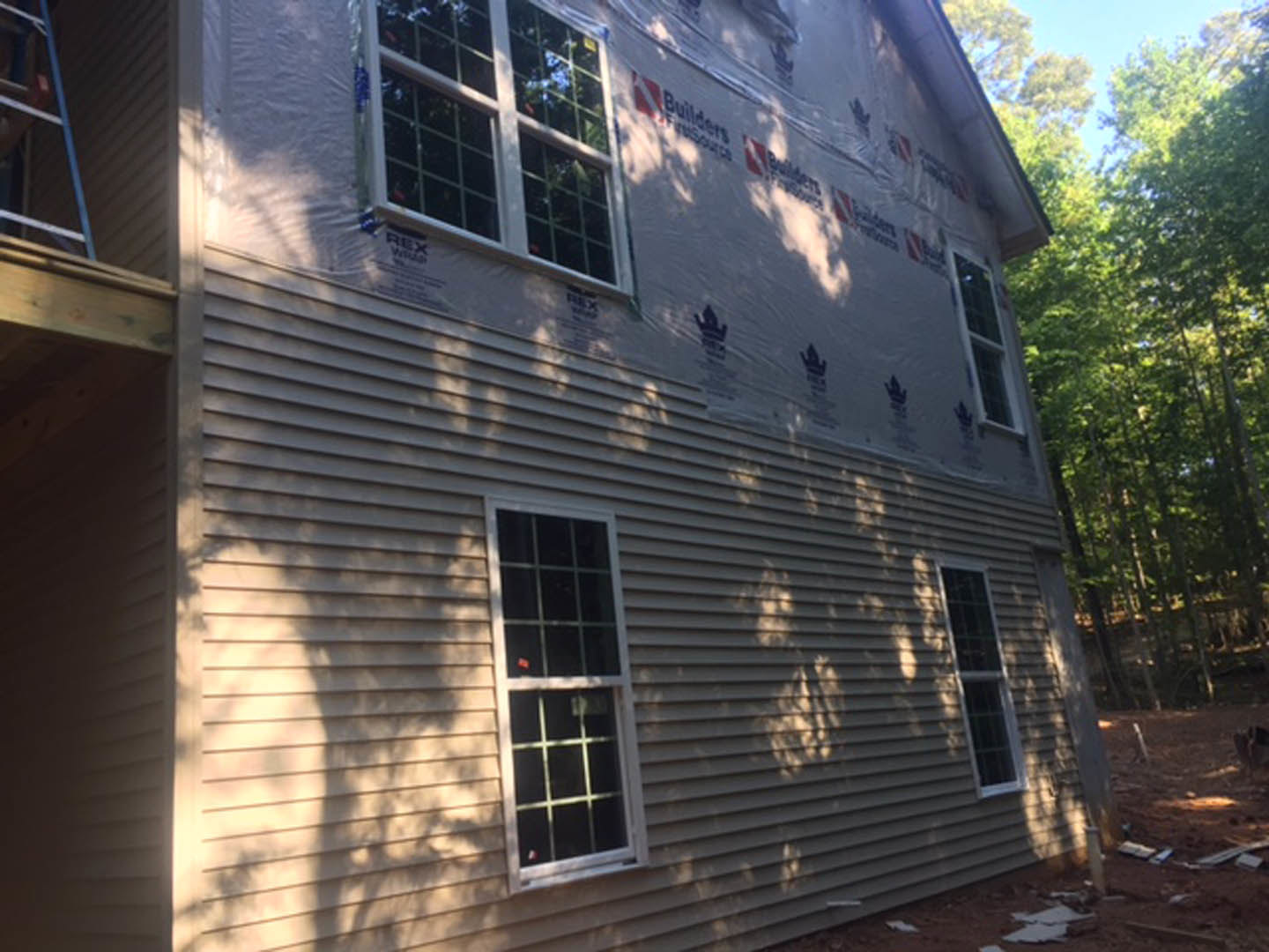 Two-story house with light-colored horizontal siding, multiple-pane sash windows, and mature trees in the background