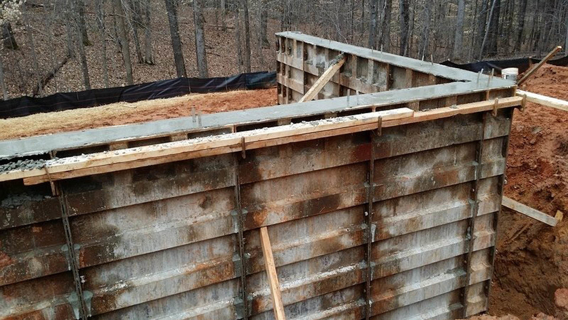 Concrete exterior wall with exposed wooden beams above ground
