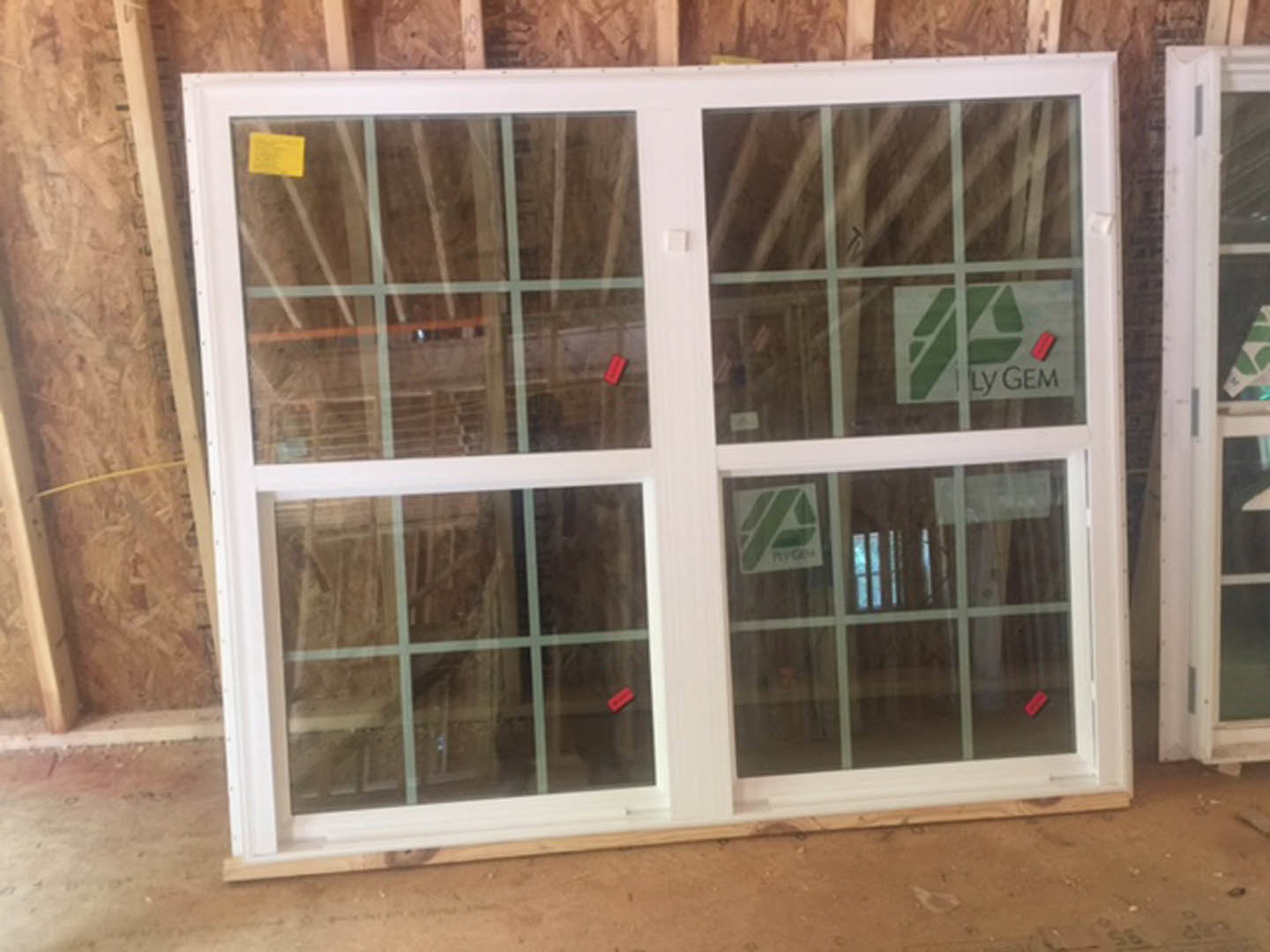 White-framed window with clear glass set in an interior wall, yellow sticker visible nearby, partial view of white door in background