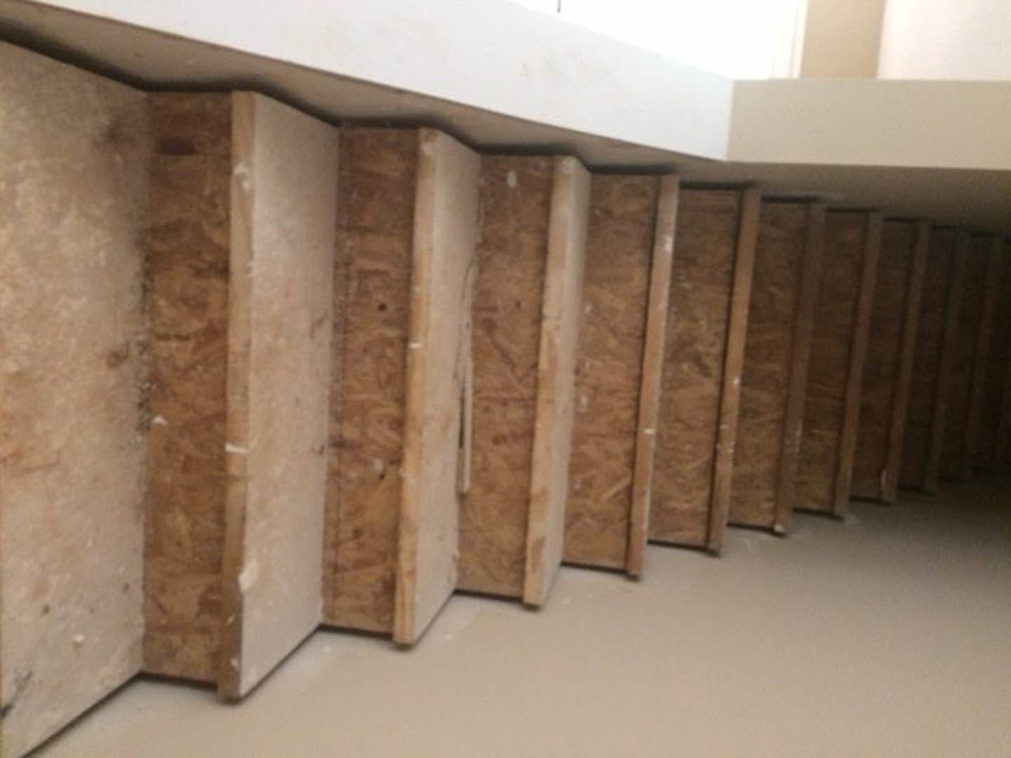 Cluster of light wood panels and boxes set against white plaster walls and stone accent, black stripe detail on smooth surface