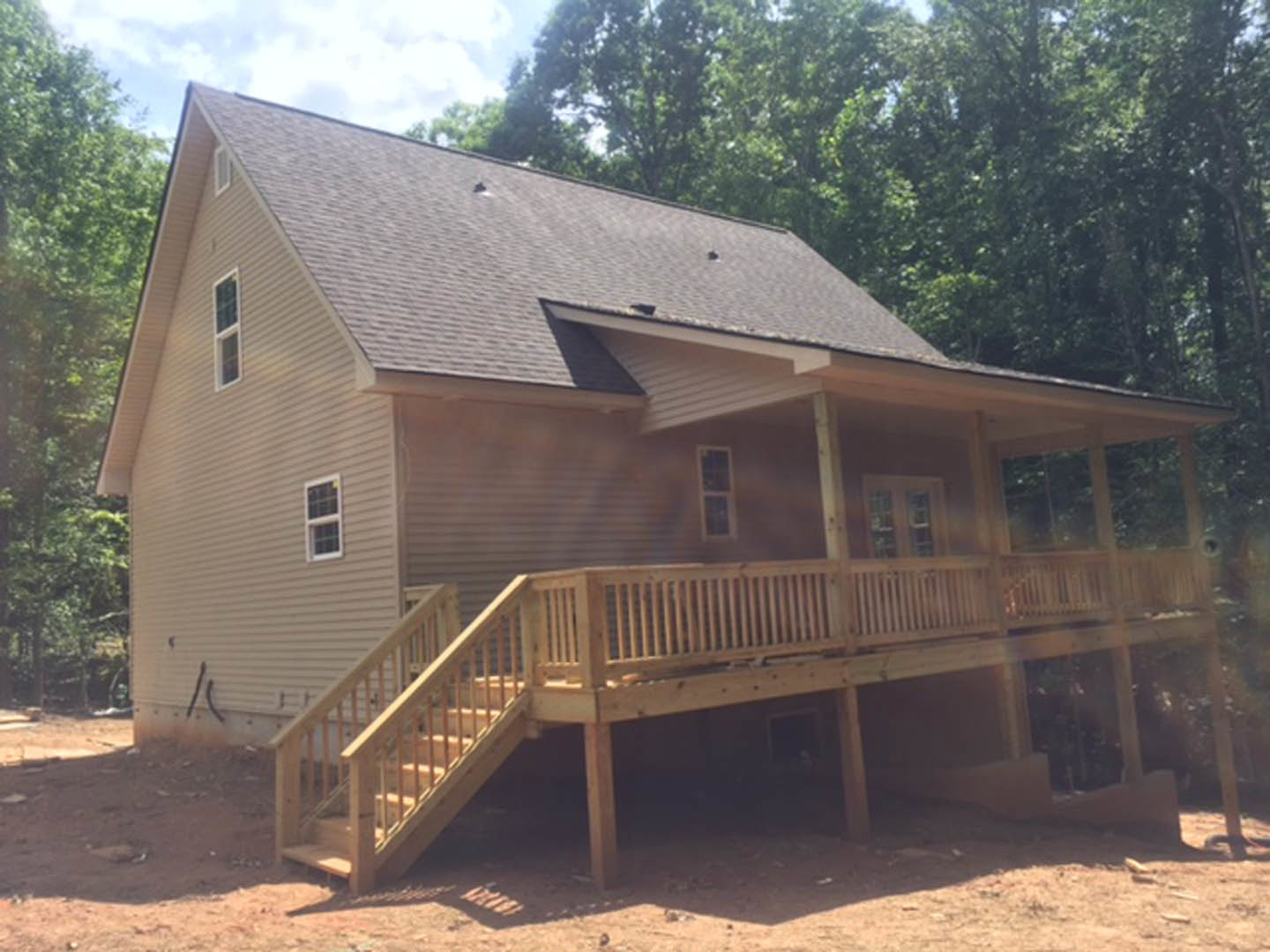 Two-story house with wooden porch and stairs, light siding, multi-pane windows, gabled roof, surrounded by trees and lawn