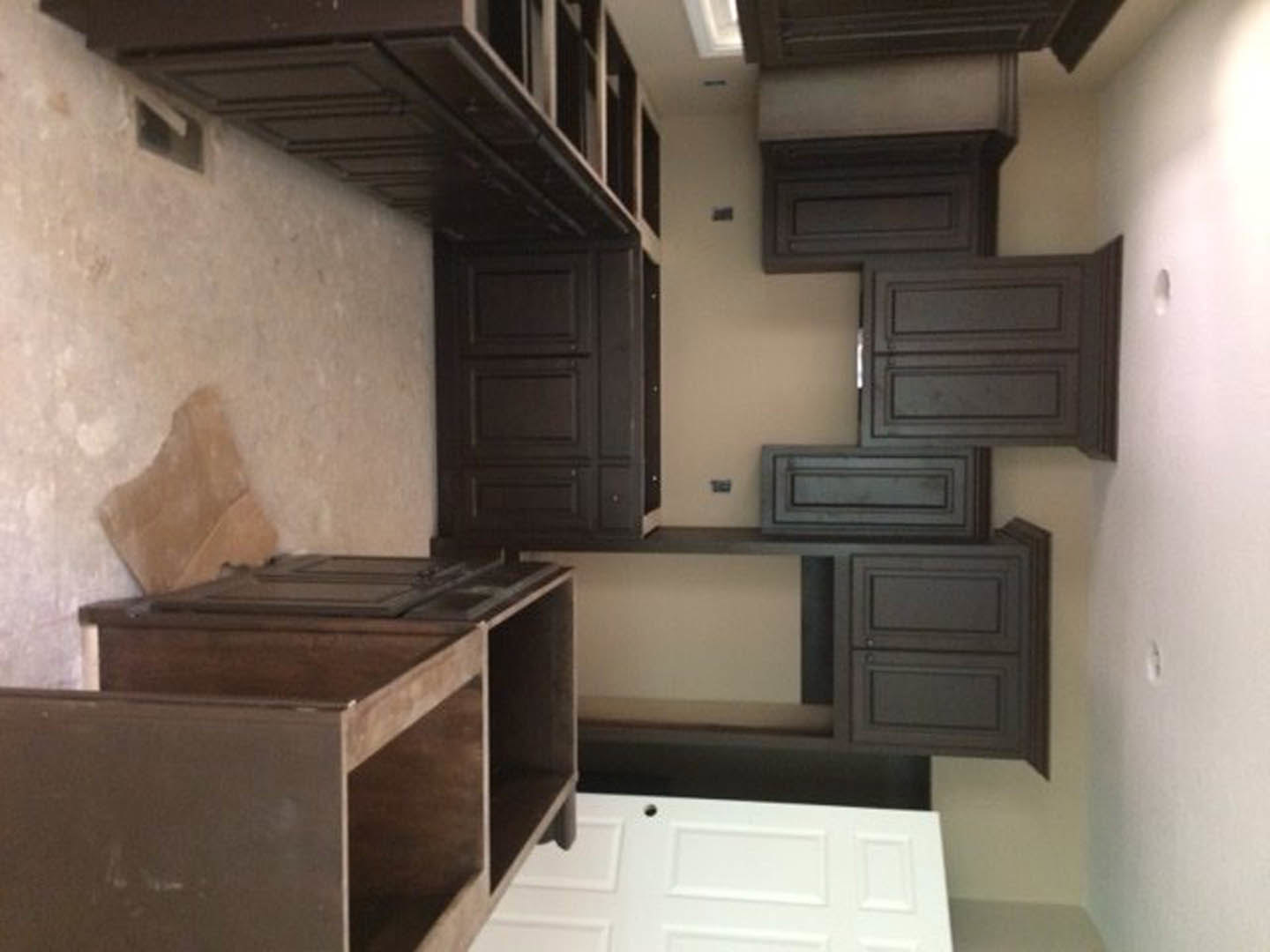 Open-concept kitchen with white cabinetry, wood drawers, built-in stovetop, and adjacent staircase featuring wooden treads and metal railing