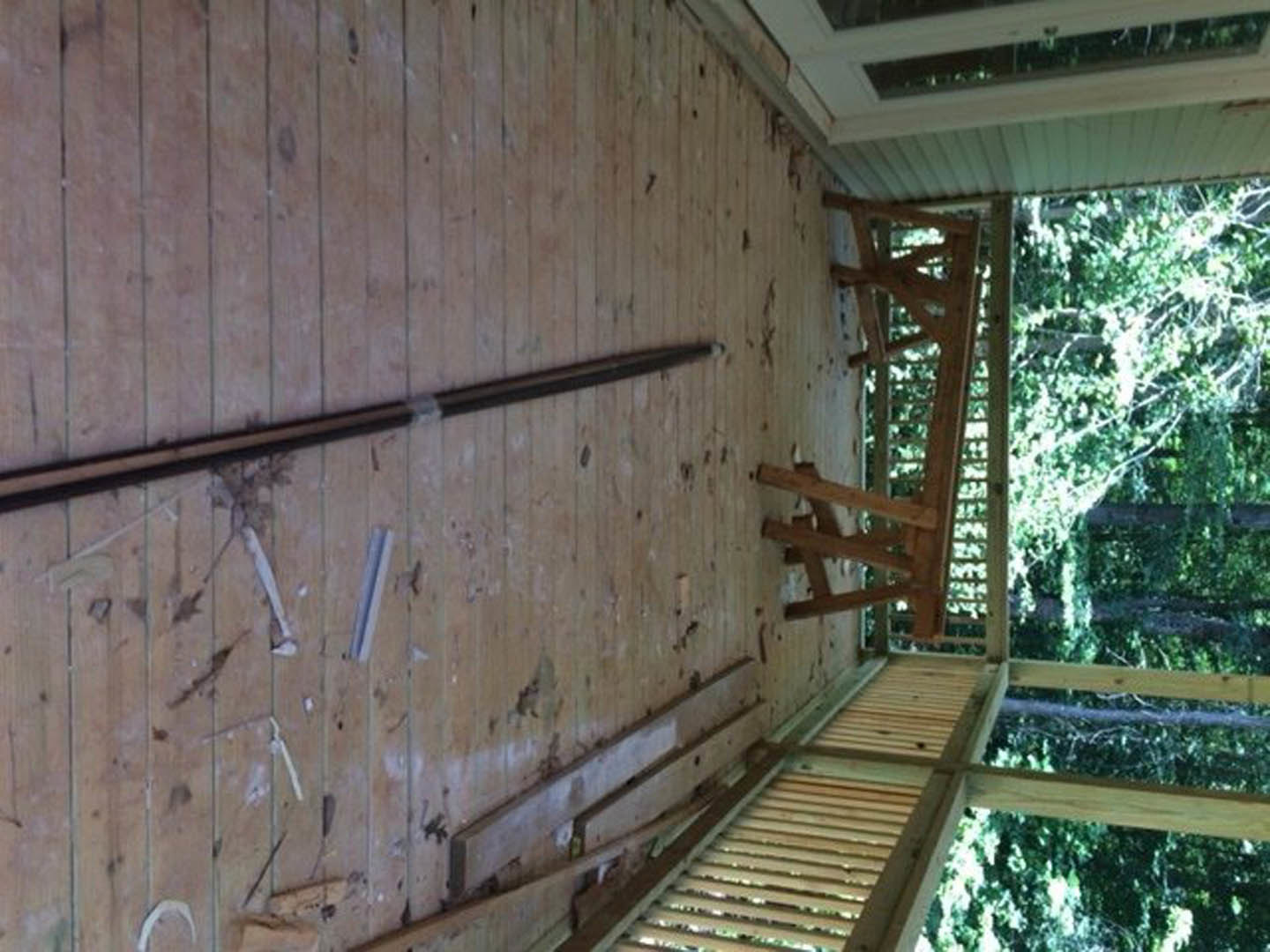 Wide-plank wood floor with exposed wood ceiling beam, large window framed by wooden trim, natural light highlighting warm wood finishes throughout the room
