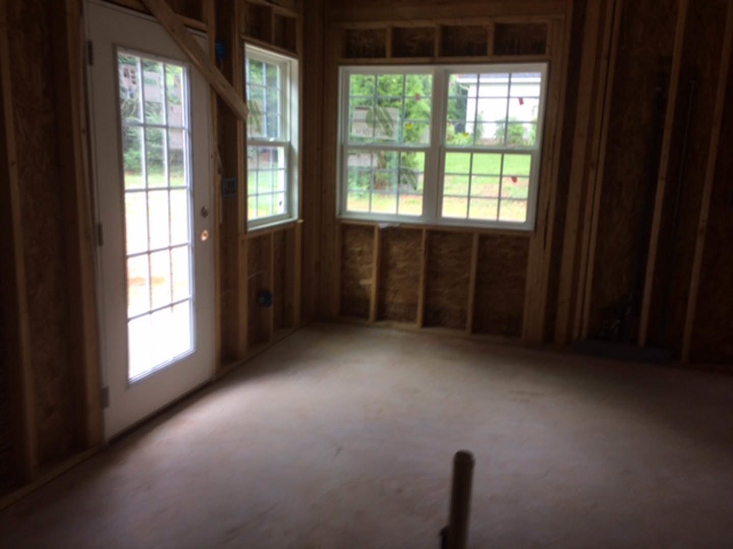 Sunlit room with multi-pane windows, hardwood plank flooring, and a white door with glass panels.