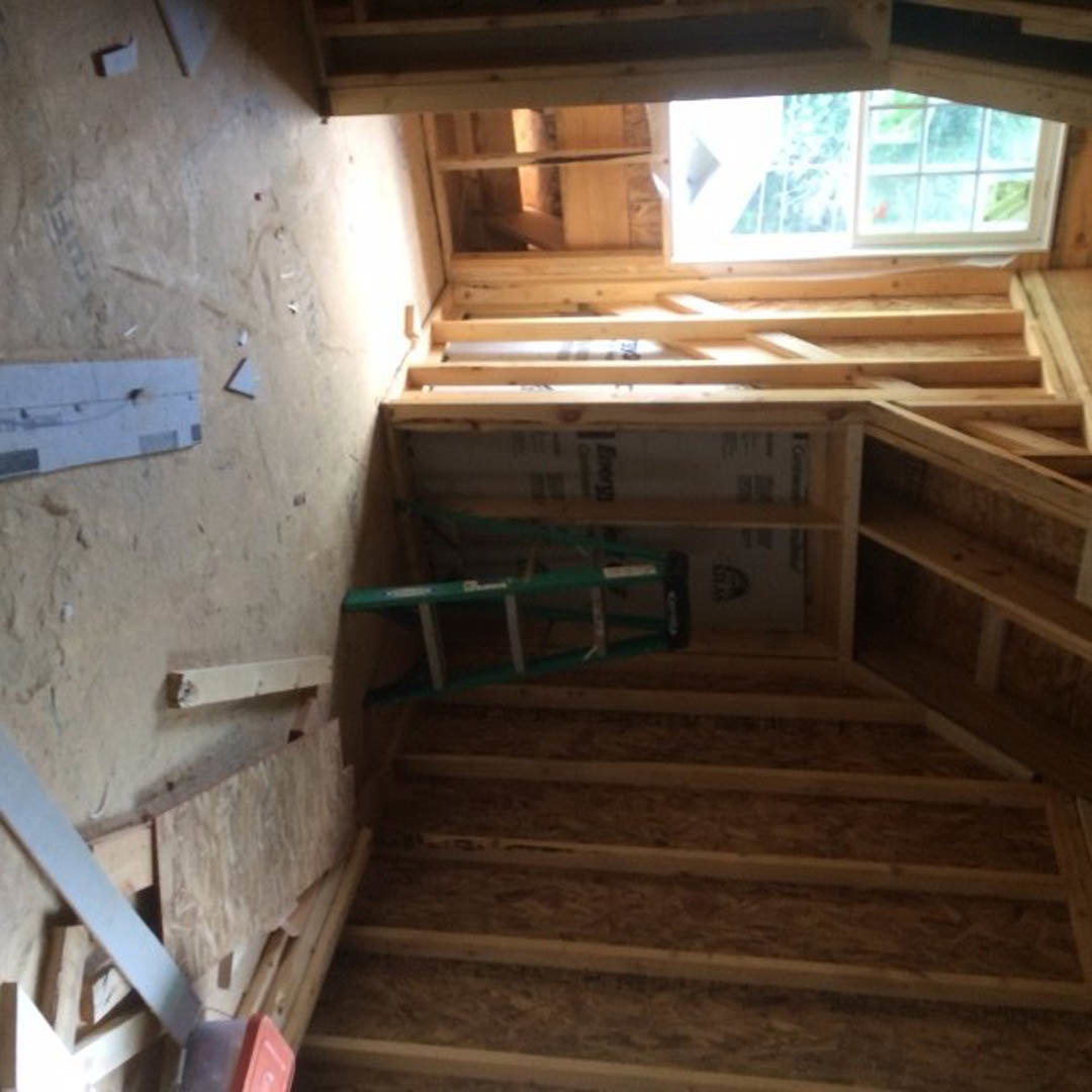 Wooden ladder leaning against unfinished wall, sunlight streaming through window onto hardwood floor, white rectangular panel with cutout visible in construction area.