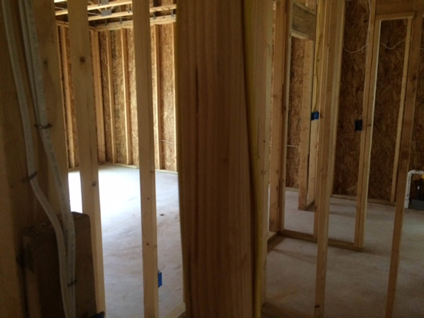 Wood-framed room under construction with exposed plywood walls, white plumbing pipes, and visible wood beams and panels