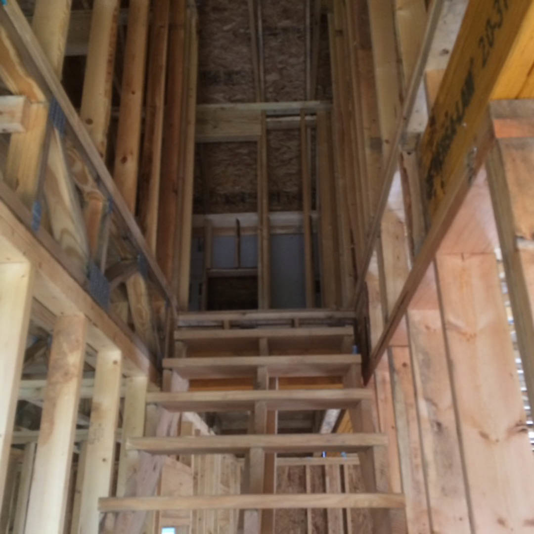Open wooden staircase with natural wood treads and risers, exposed beams, and plank flooring in a bright residential interior.