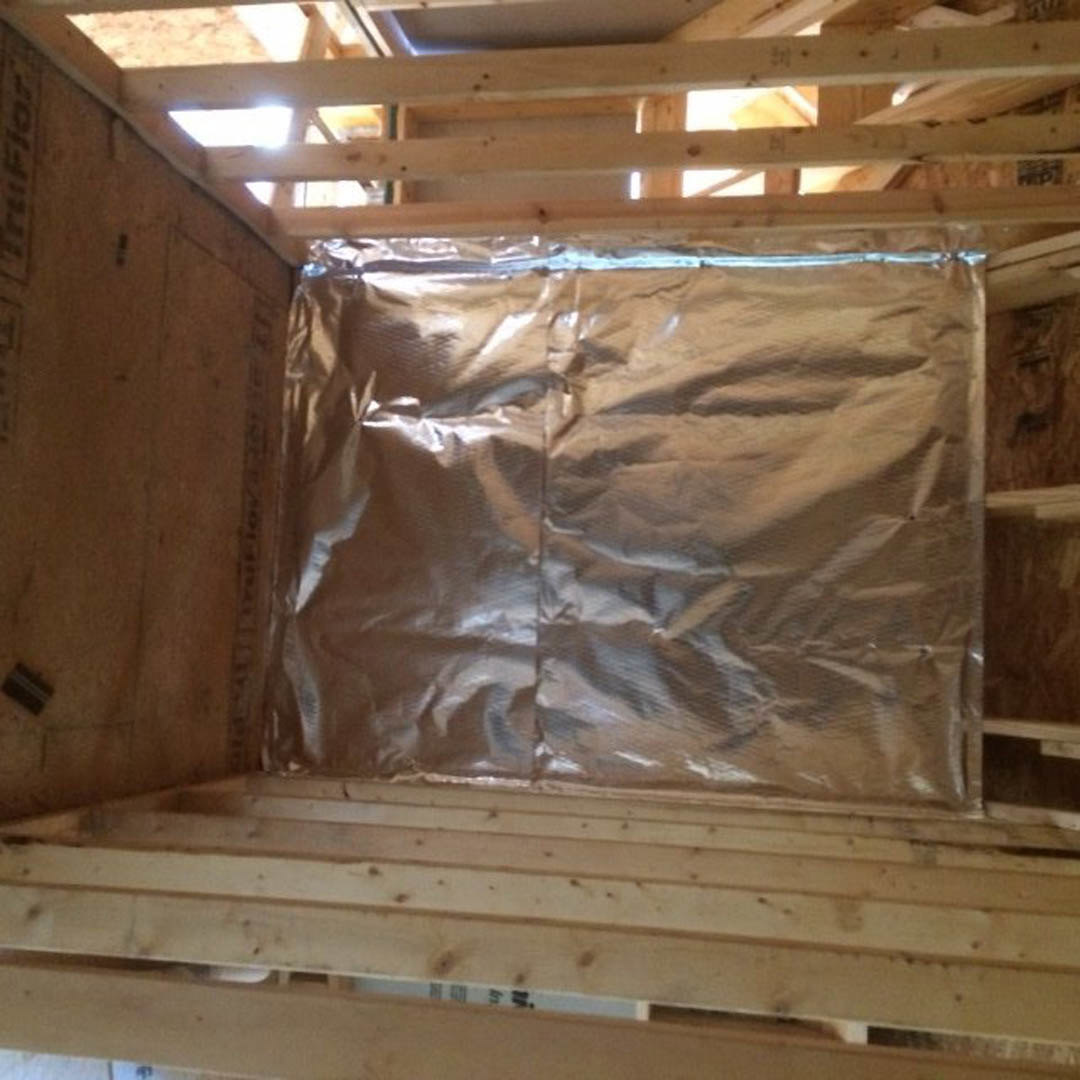 Wood-framed ceiling with exposed metal sheet insulation and visible lumber beams in an unfinished room