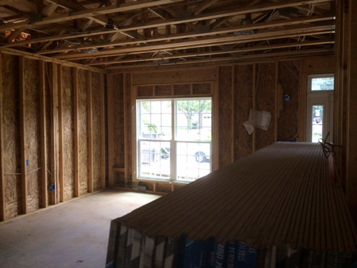 Living room with exposed wood ceiling beams, white-framed window, stacked books on a side table, television mounted on the wall, and a blurred upholstered chair in the foreground.