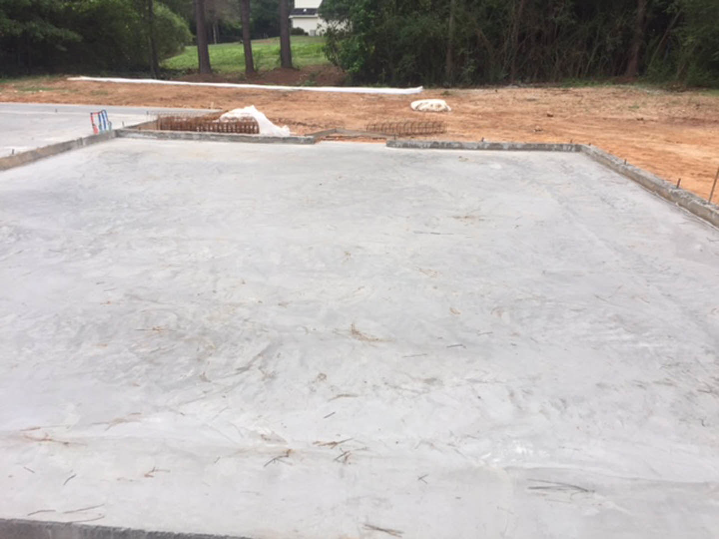 White concrete slab surrounded by a metal fence, bordered by green grass and trees in the background