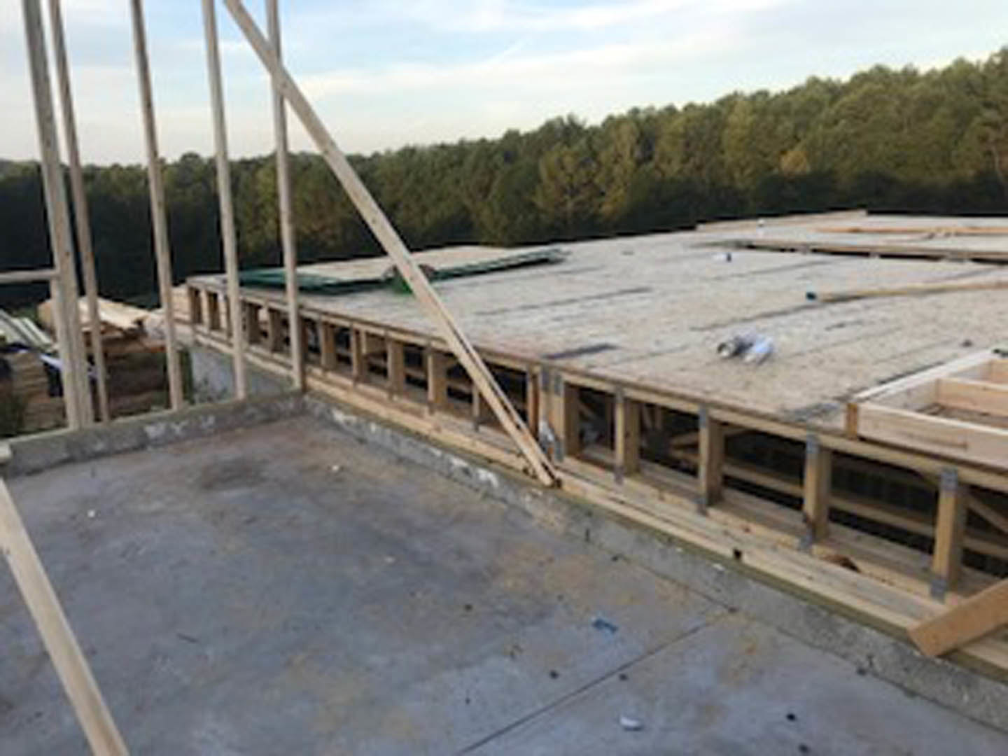 Wood-framed custom home under construction on concrete foundation, surrounded by trees and open sky