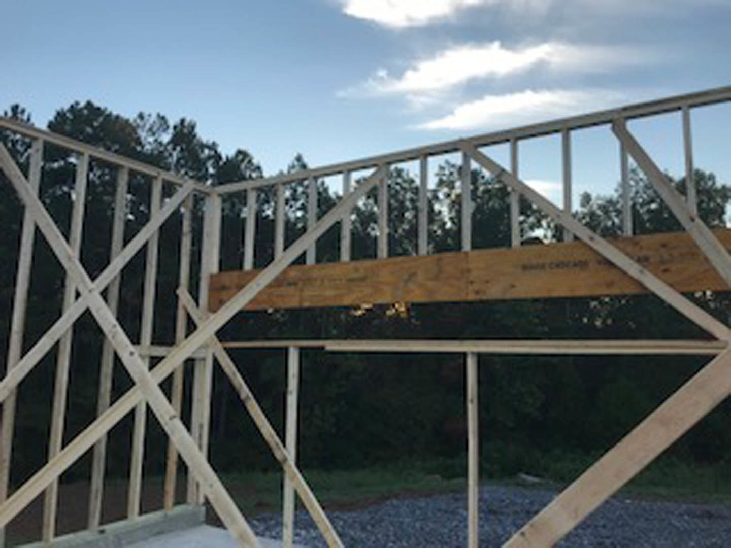 Exposed wooden beam and post on outdoor deck with cloudy sky and trees in background