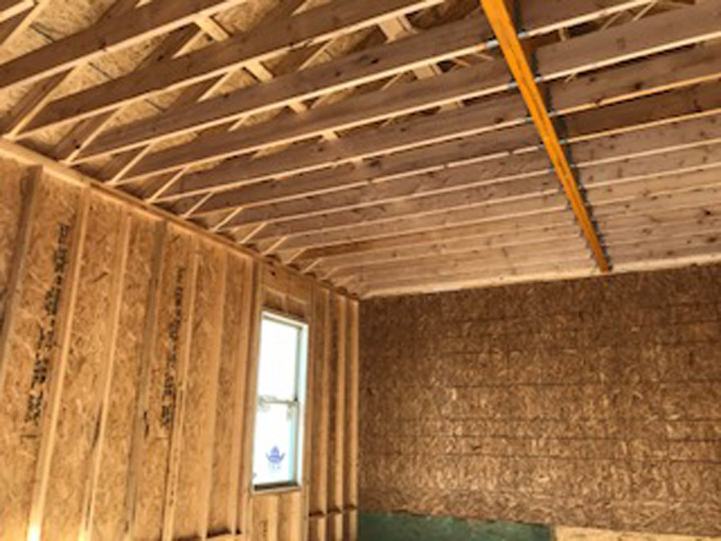 Wooden ceiling with exposed beams, straw-insulated wall, wood paneling, window letting in natural light