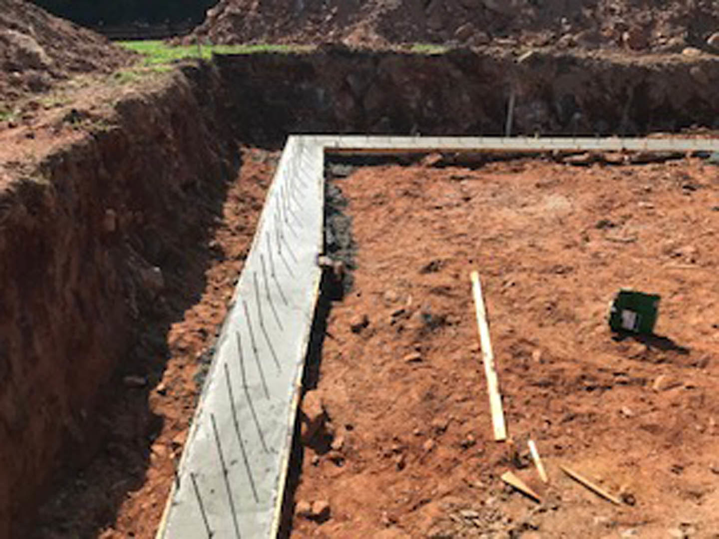 Wooden walkway crossing dirt foundation at outdoor construction site with soil and mountain backdrop