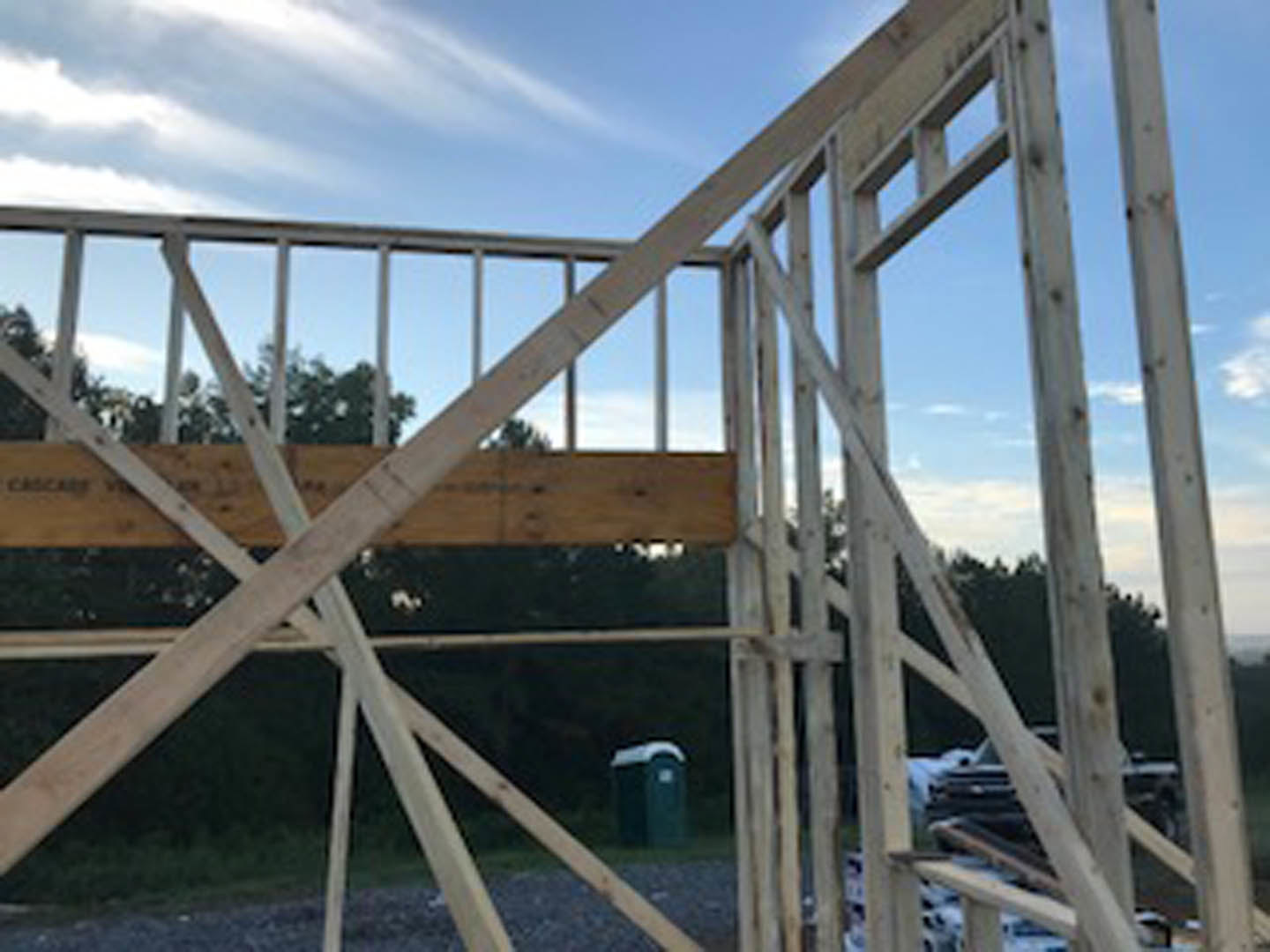 Exposed wooden framing of a house under construction with lumber beams, open walls, and blue sky in the background