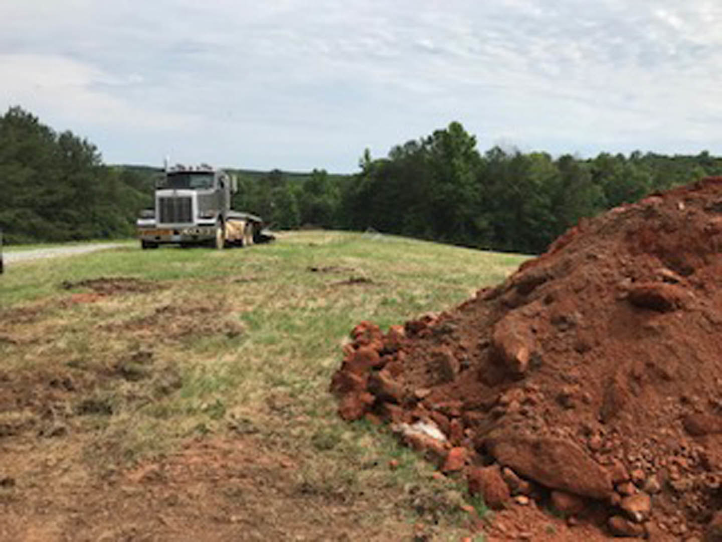 White pickup truck parked atop a dirt mound in grassy field, surrounded by trees under cloudy sky
