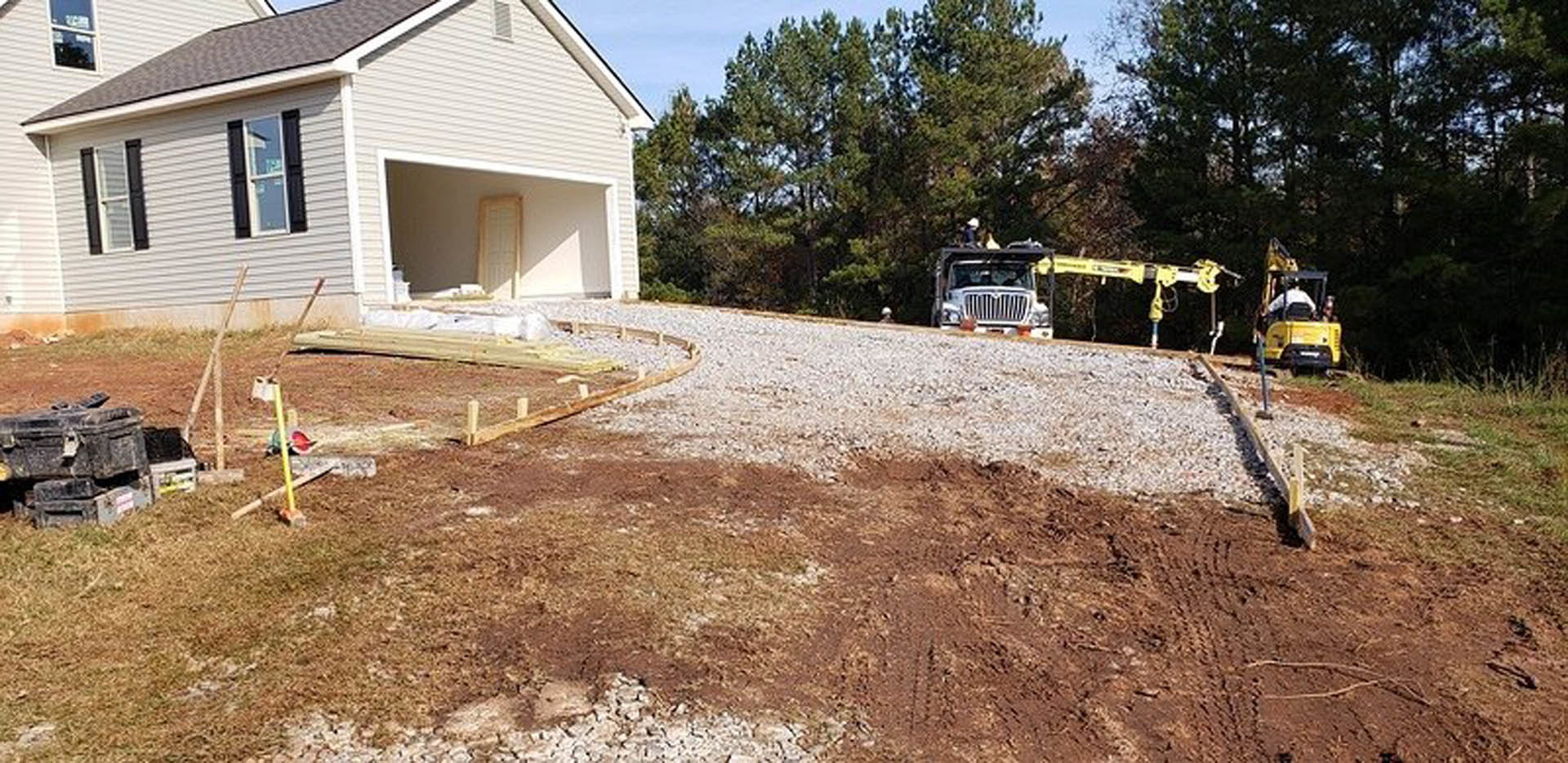 White pickup truck parked on concrete driveway in front of modern two-story home with gray siding, large windows, and landscaped lawn with trees and shrubs