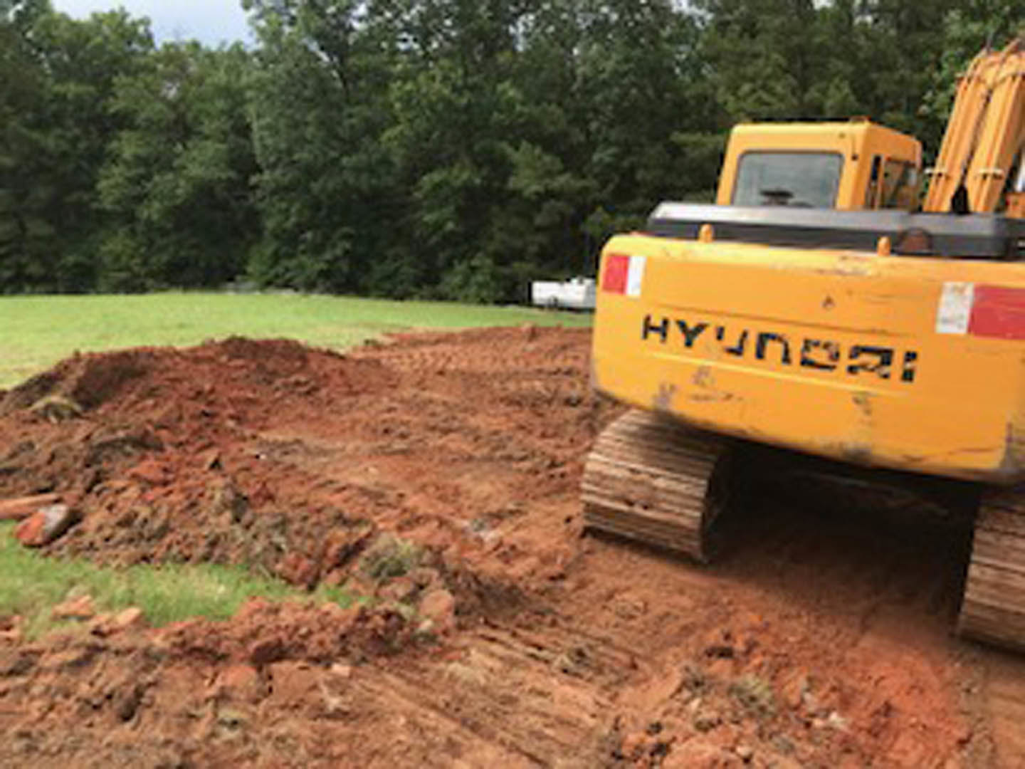 Yellow bulldozer with large wheels parked on dirt field, surrounded by trees and open sky