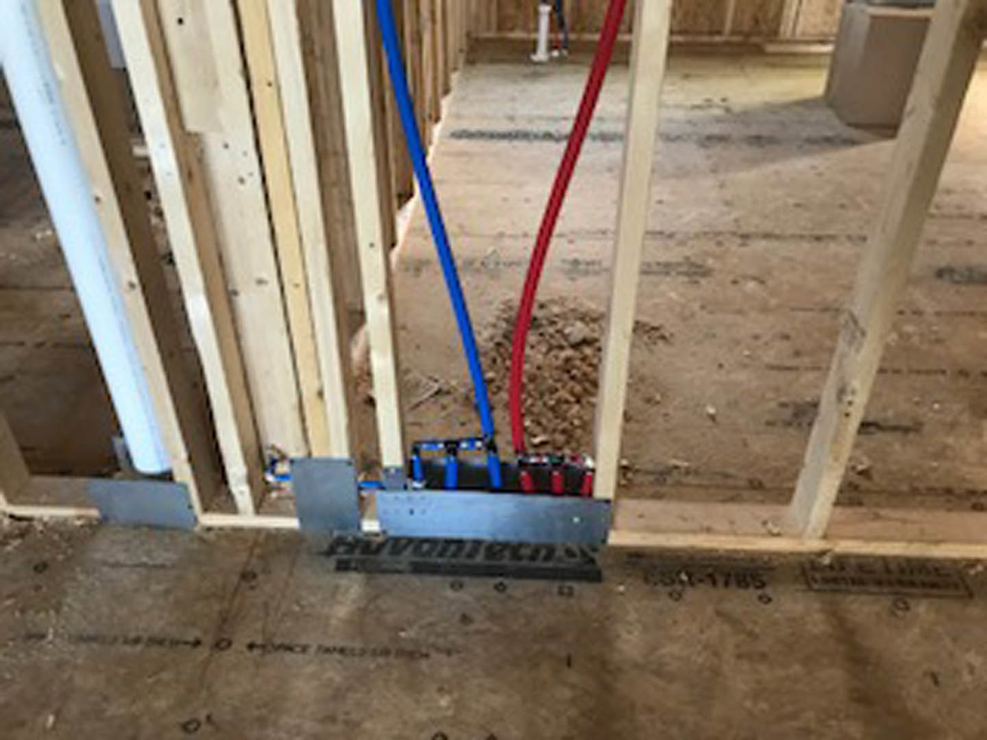 Blue and red water supply pipes emerging from a hole in a drywall, surrounded by unfinished composite material during home remodel.
