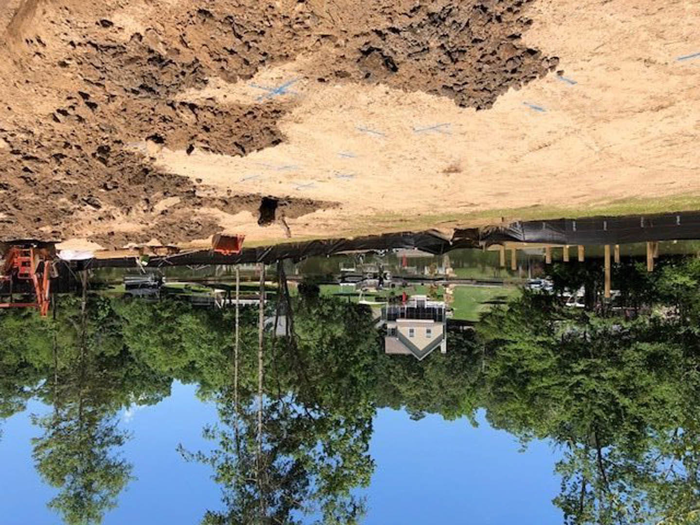 Dirt road lined with trees leading to a house with a gabled roof in the background, surrounded by natural landscape and vegetation